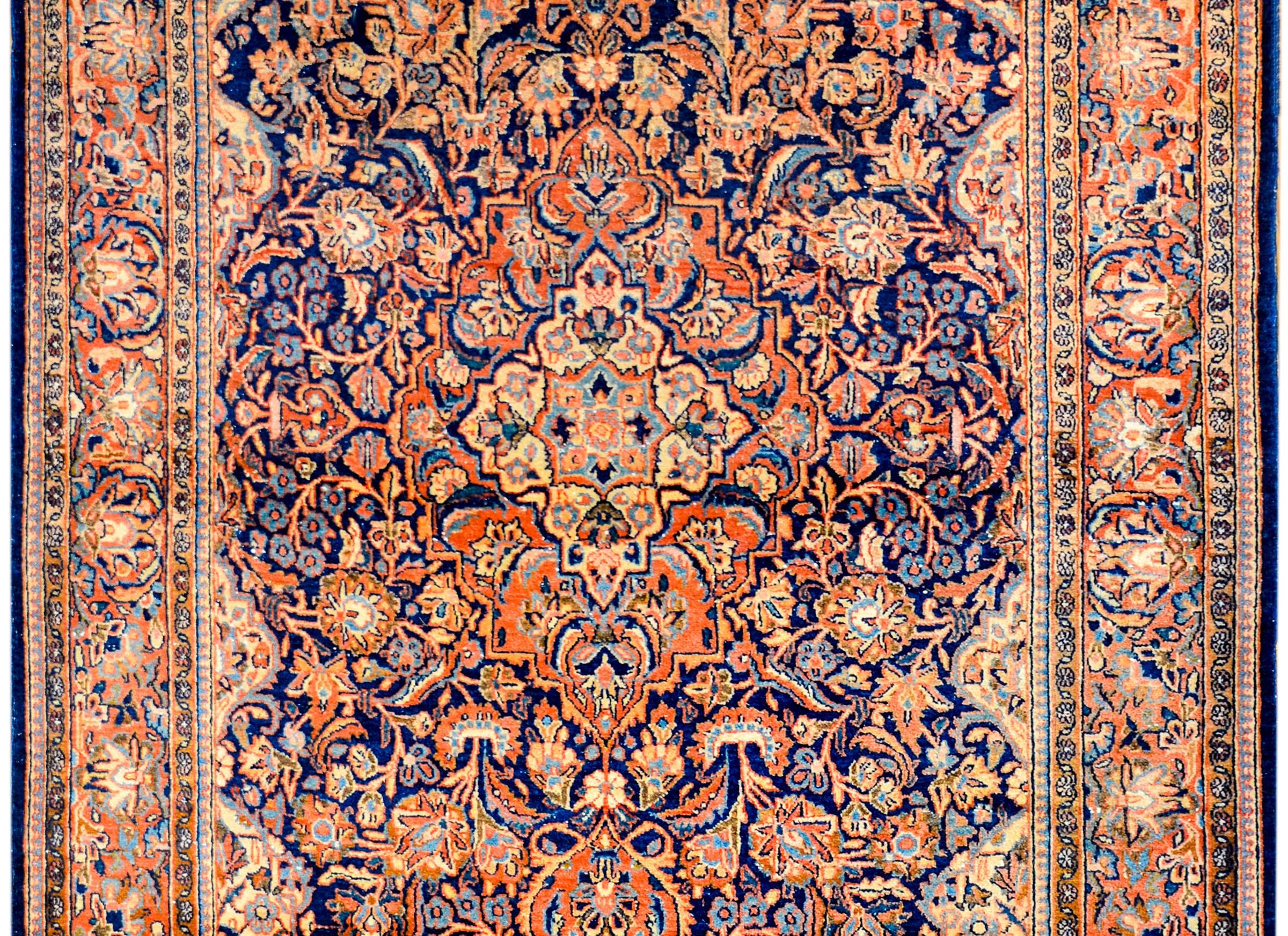 A wonderful early 20th century Persian Kashan rug with a densely woven field and medallion of myriad flowers, leaves, and vines, all woven in orange, indigo, gold, and cream colored vegetable dyed wool. The border is complex and as densely woven as