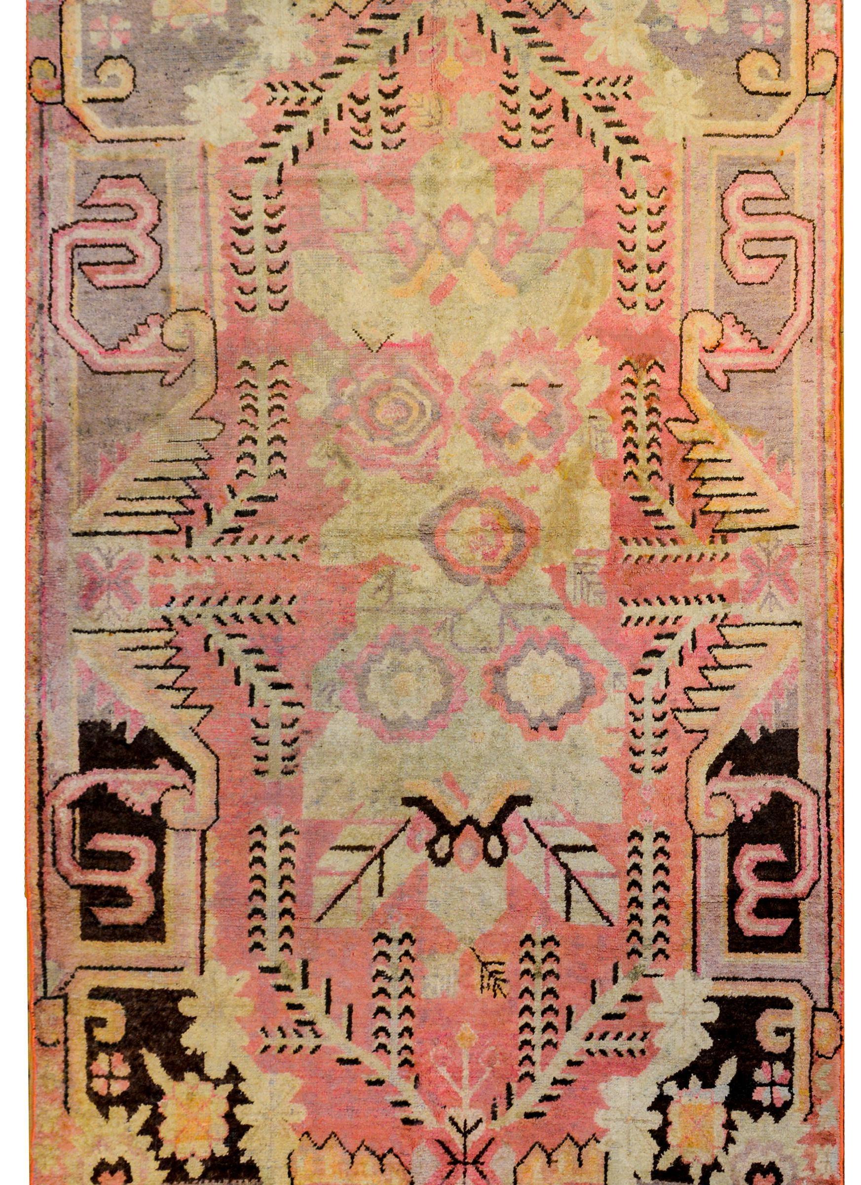 An incredible early 20th century Central Asian Khotan rug with a bold, large scale, floral and leaf pattern medallion woven in link, lavender, sherbet, and pal green, on a pink background, surrounded by a baroque floral and leaf patterned border.