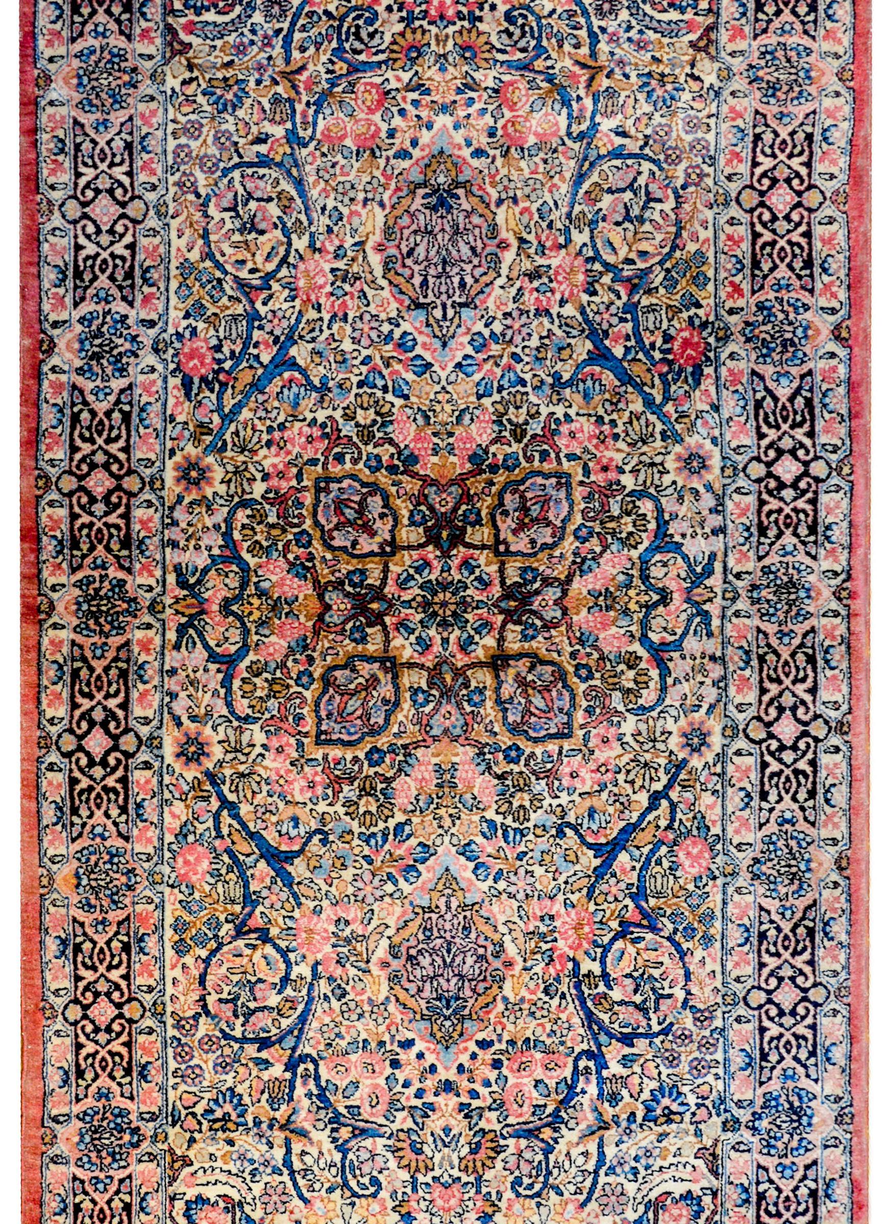 A wonderful early 20th century Persian Kirman rug with a densely woven mirrored scrolling vine and floral pattern woven in traditional Kirman colors of light and dark indigo, pink, and gold, on a cream colored background. The central medallion is a