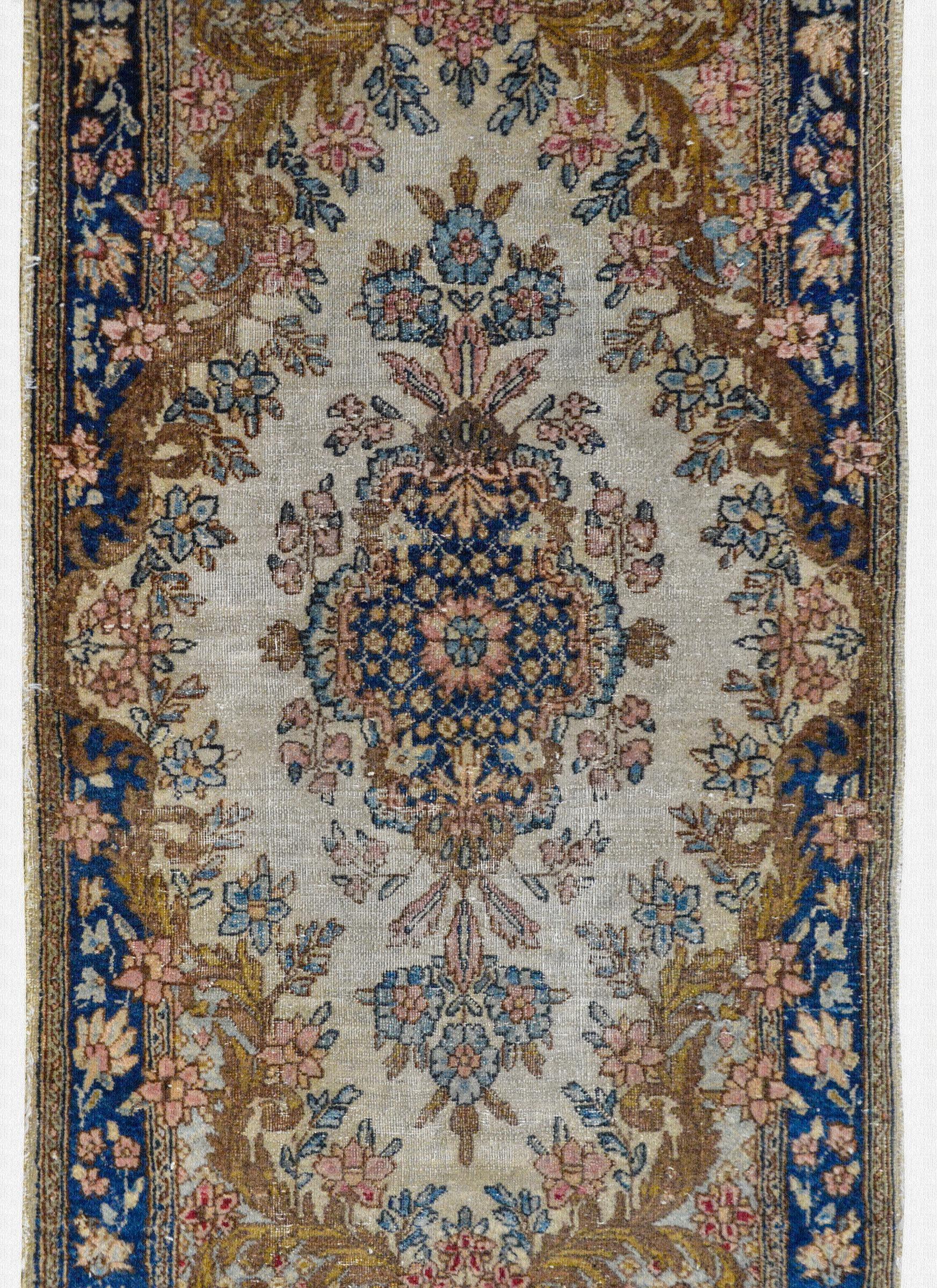 A wonderful early 20th century Persian Kirman rug with a large central floral medallion woven in traditional Kiram colors of indigo, pink, brown, and cream, surrounded by an elaborately woven border with additional flowers and scrolling leaves.