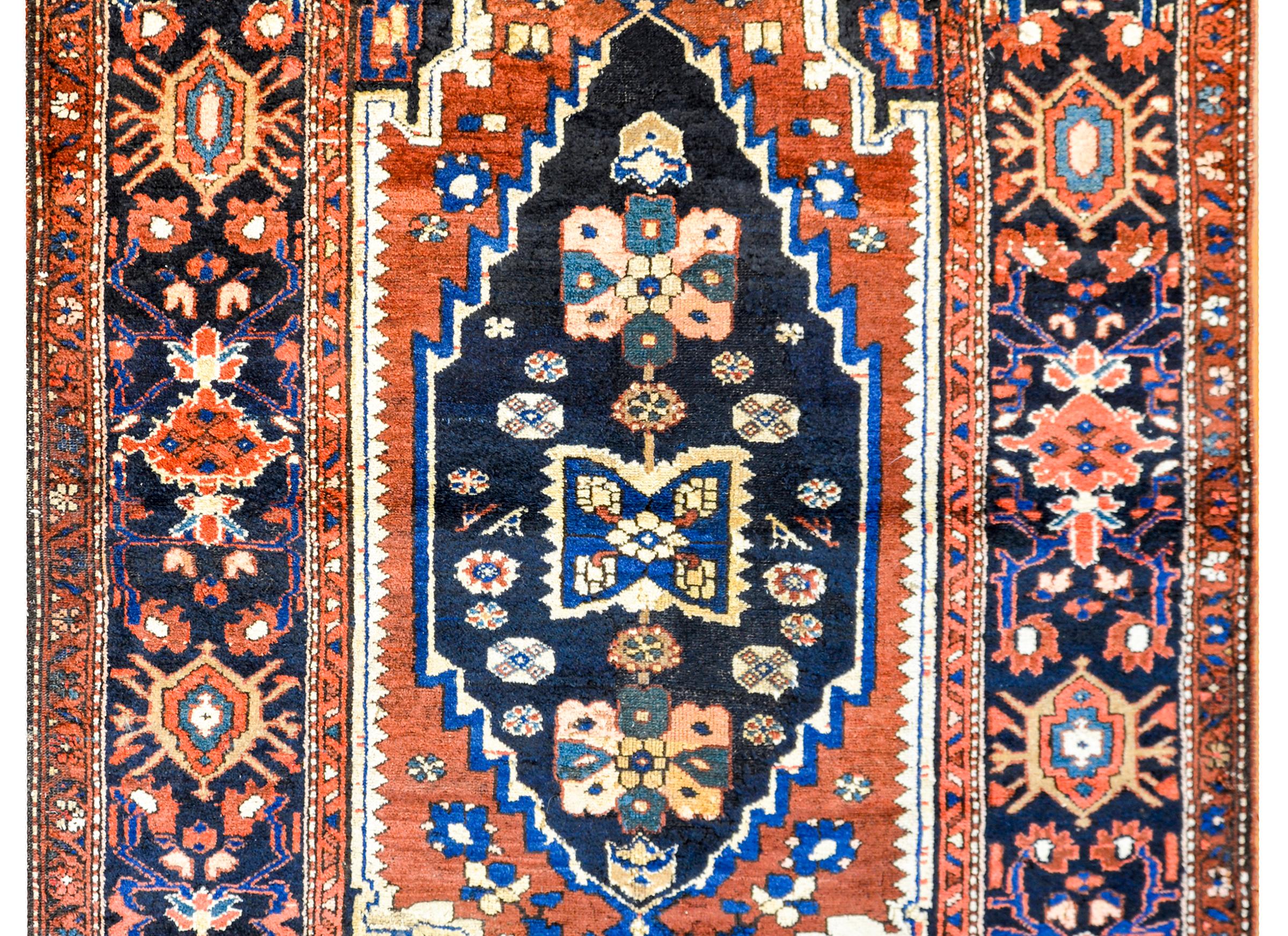 A wonderful early 20th century Persian Lori rug with a fantastic bold tribal pattern containing a large diamond medallion with several stylized floral patterns on a dark indigo background surronded by a crimson ground. The border is beautiful, with