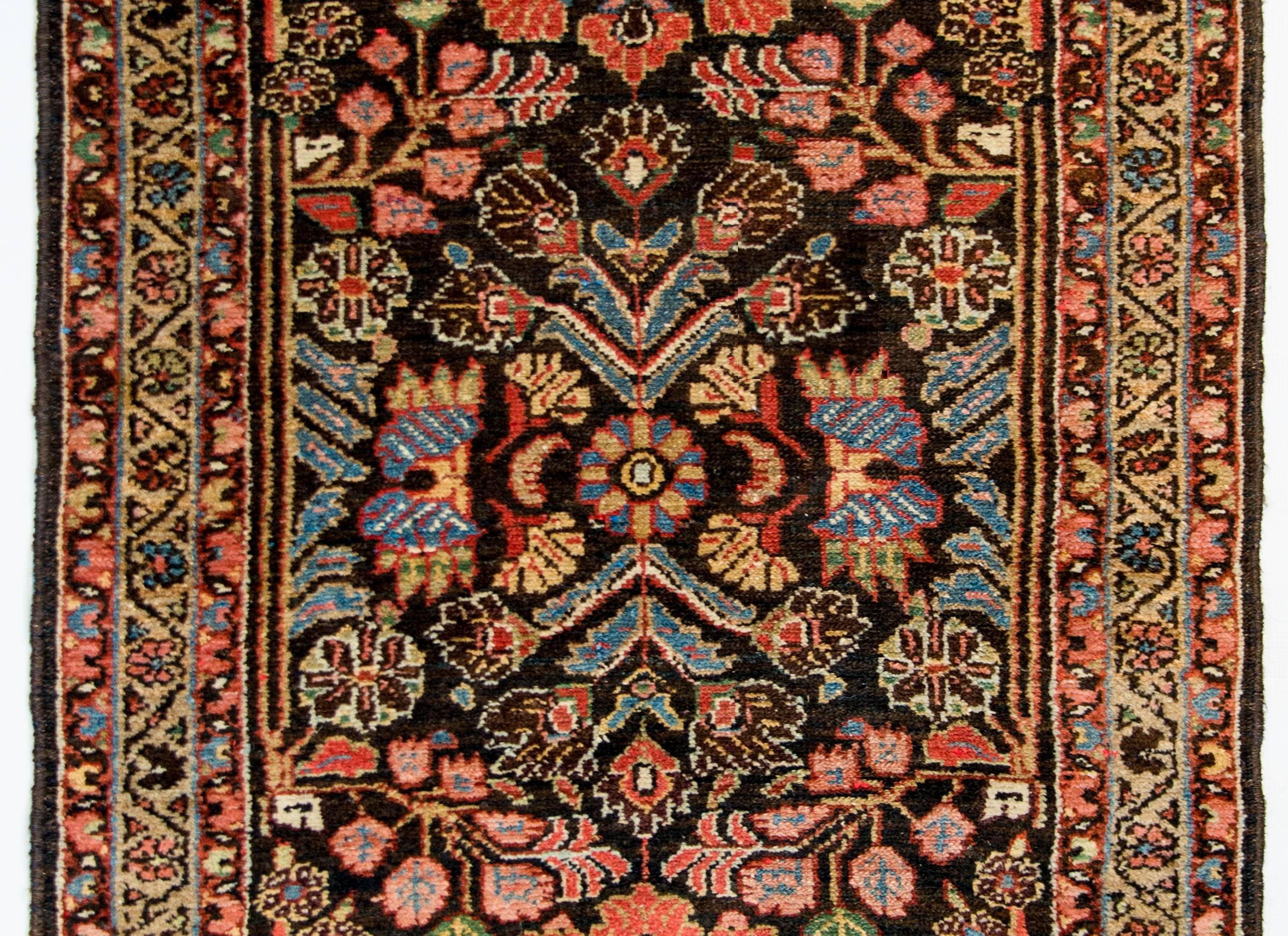 A fantastic early 20th century Persian Malayer rug with a mirrored multicolored floral and leaf pattern woven in indigo, crimson, pink, green, and white on a dark indigo background. The border is composed with one central floral stripe on a gold