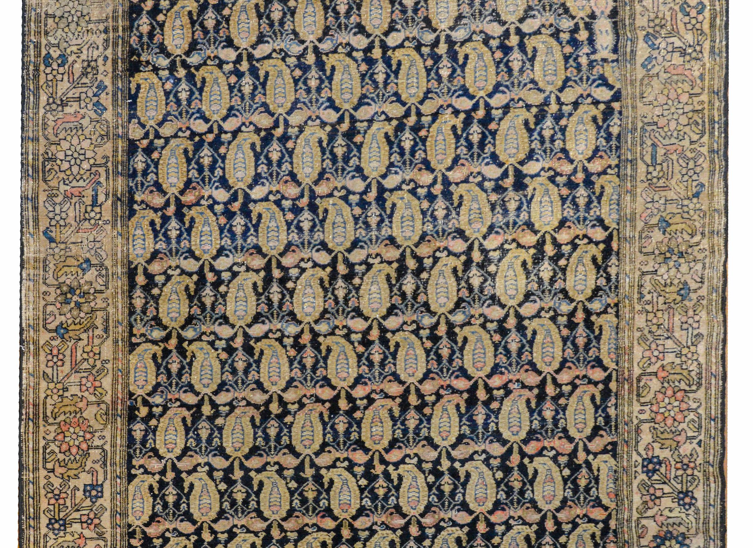 A wonderful early 20th century Persian Malayer rug with an allover paisley and petite floral pattern woven in pale green, light indigo, pink, and gold vegetable dyed wool on a dark indigo background, surrounded by a fantastic wide large-scale floral