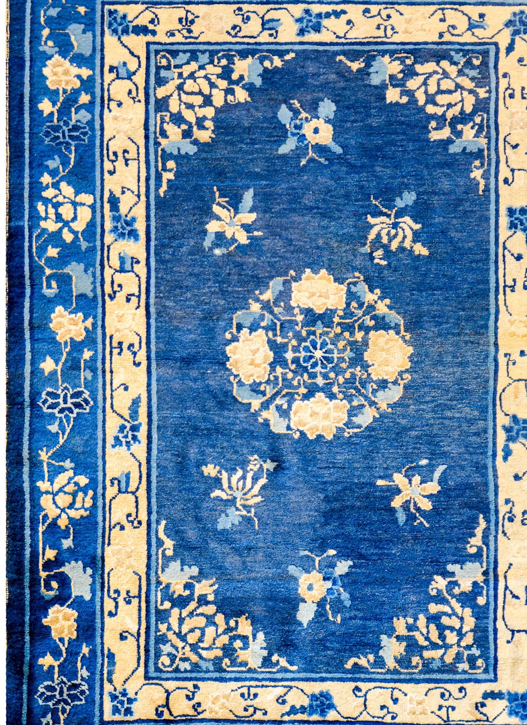 A wonderful early 20th century Peking rug woven in a fantastic indigo and cream color-way, with a large central peony and butterfly medallion amidst a field of chrysanthemums. The border is complex with two distinct peony and leafy vine patterned