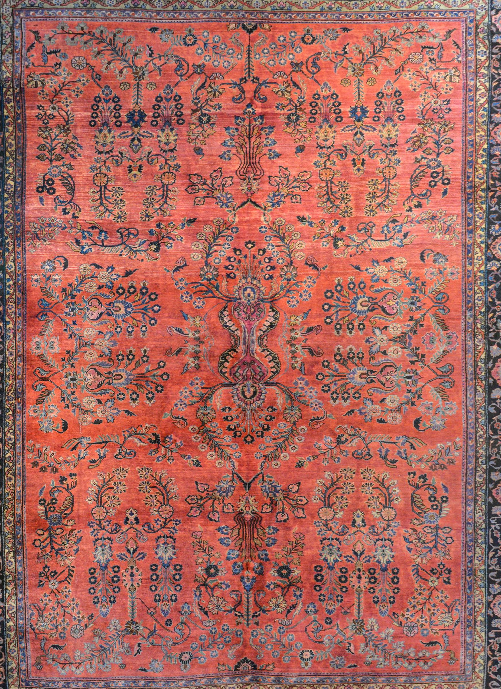 A wonderful early 20th century Persian Sarouk Mahajeran rug with a wonderful all-over mirrored floral pattern woven in light and dark indigo, cream, and pink on a rich coral background. The border is exquisite with a beautifully scrolled floral and