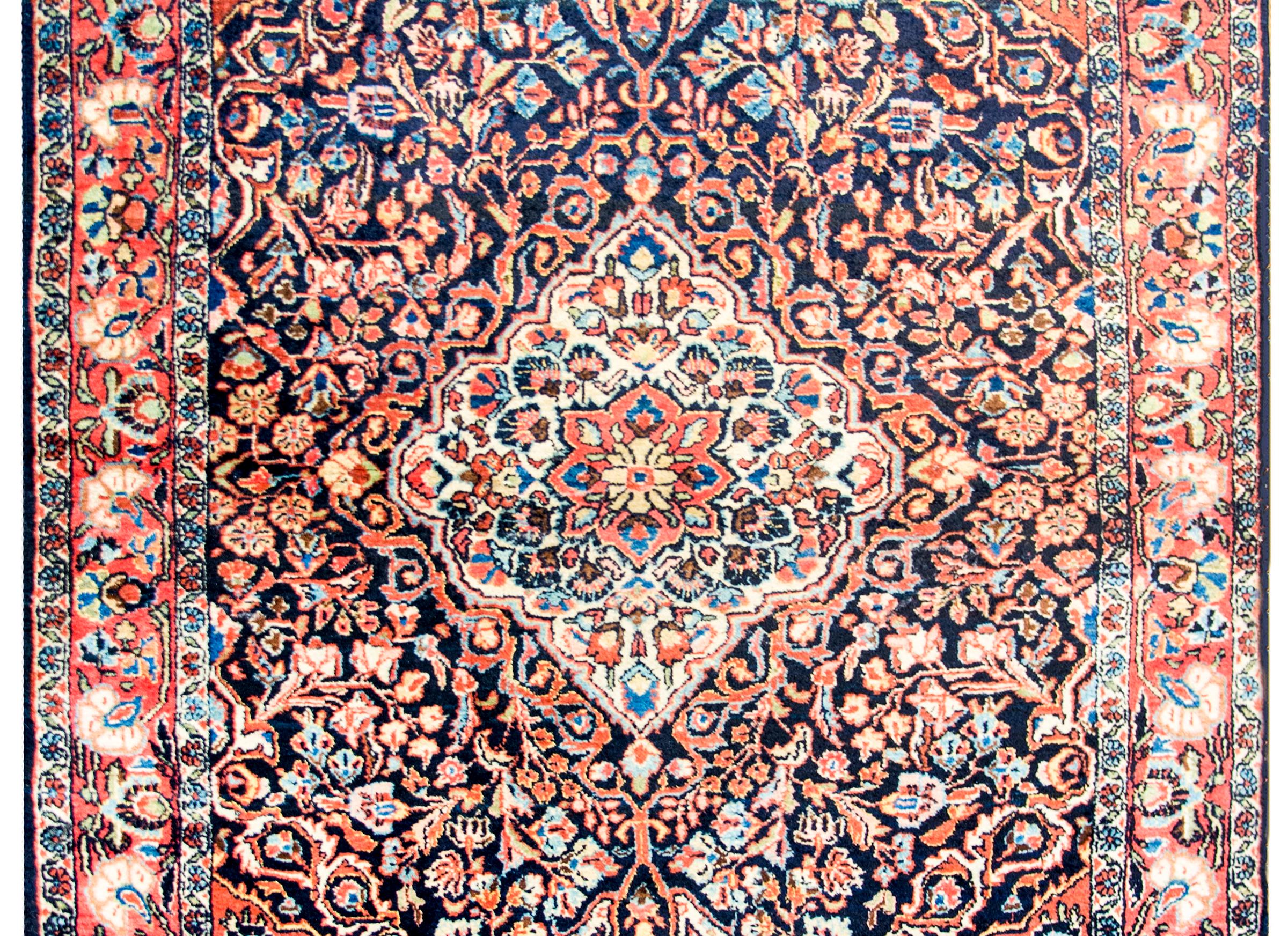A wonderful early 20th century, Persian Sarouk rug with an exceptionally beautiful pattern containing a large central diamond medallion, amidst a field of all-over mirrored scrolling vines and flowers woven in crimson, pink, cream, and light indigo