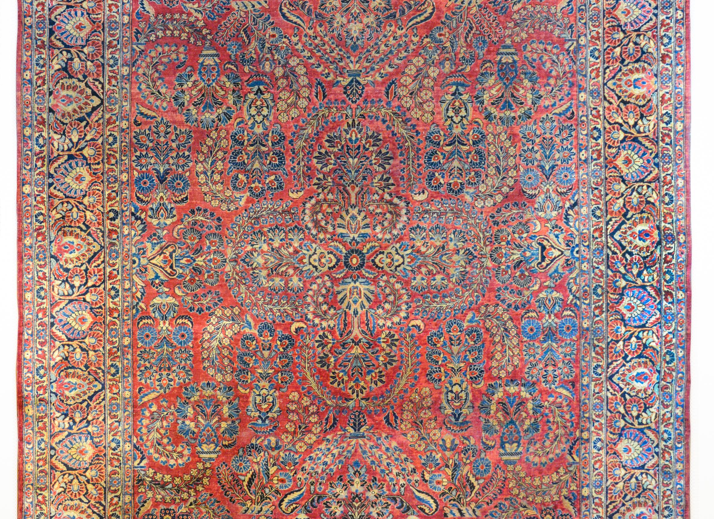 A wonderful early 20th century Persian Sarouk rug with an all-over mirrored floral pattern, woven in light and dark indigo, cream, and pink, all against a rich cranberry background. The border is wide, composed with multiple floral partnered