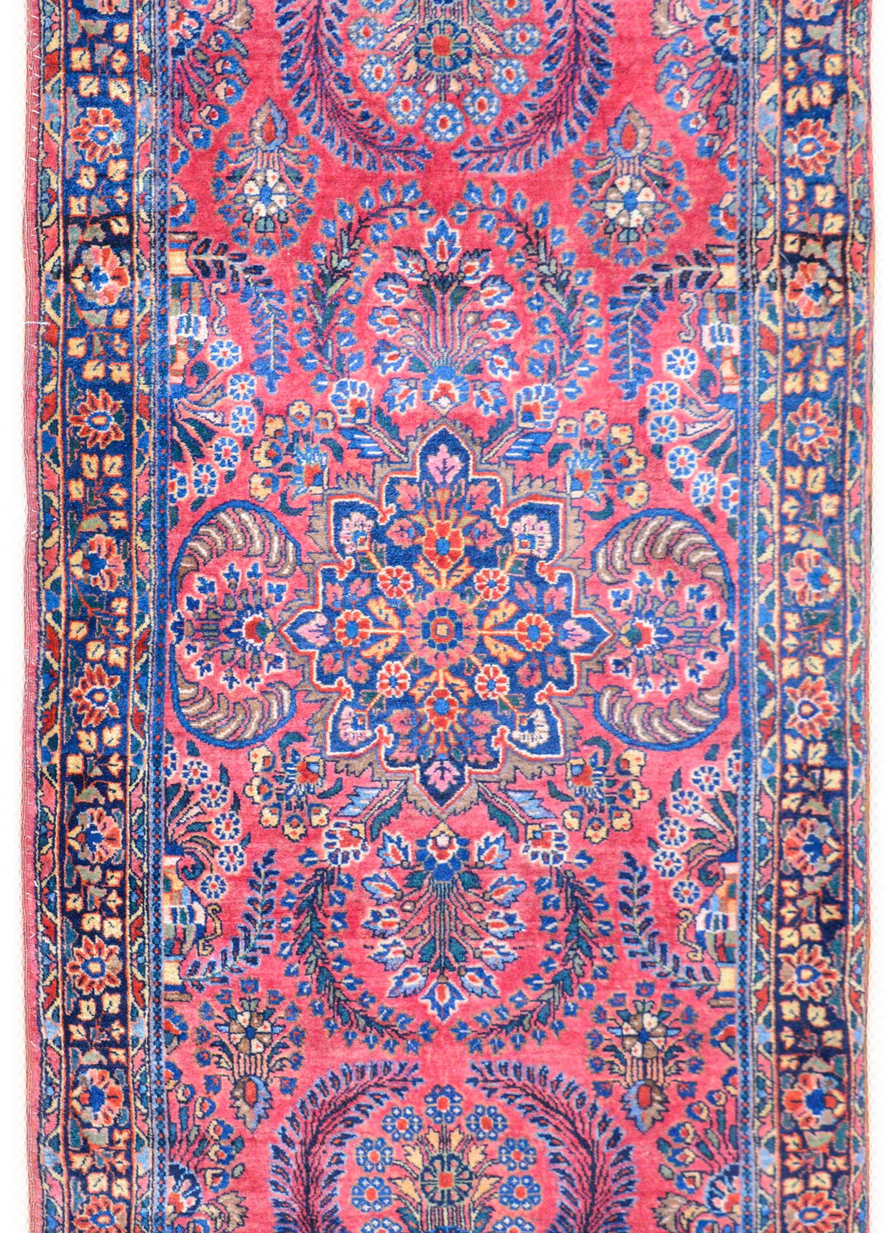 A wonderful early 20th century Persian Sarouk rug with an incredible large floral medallion in a large-scale mirrored scrolling vine and leaf pattern woven in light and dark indigo, cream, gold, and pink, against a rich cranberry field. The border