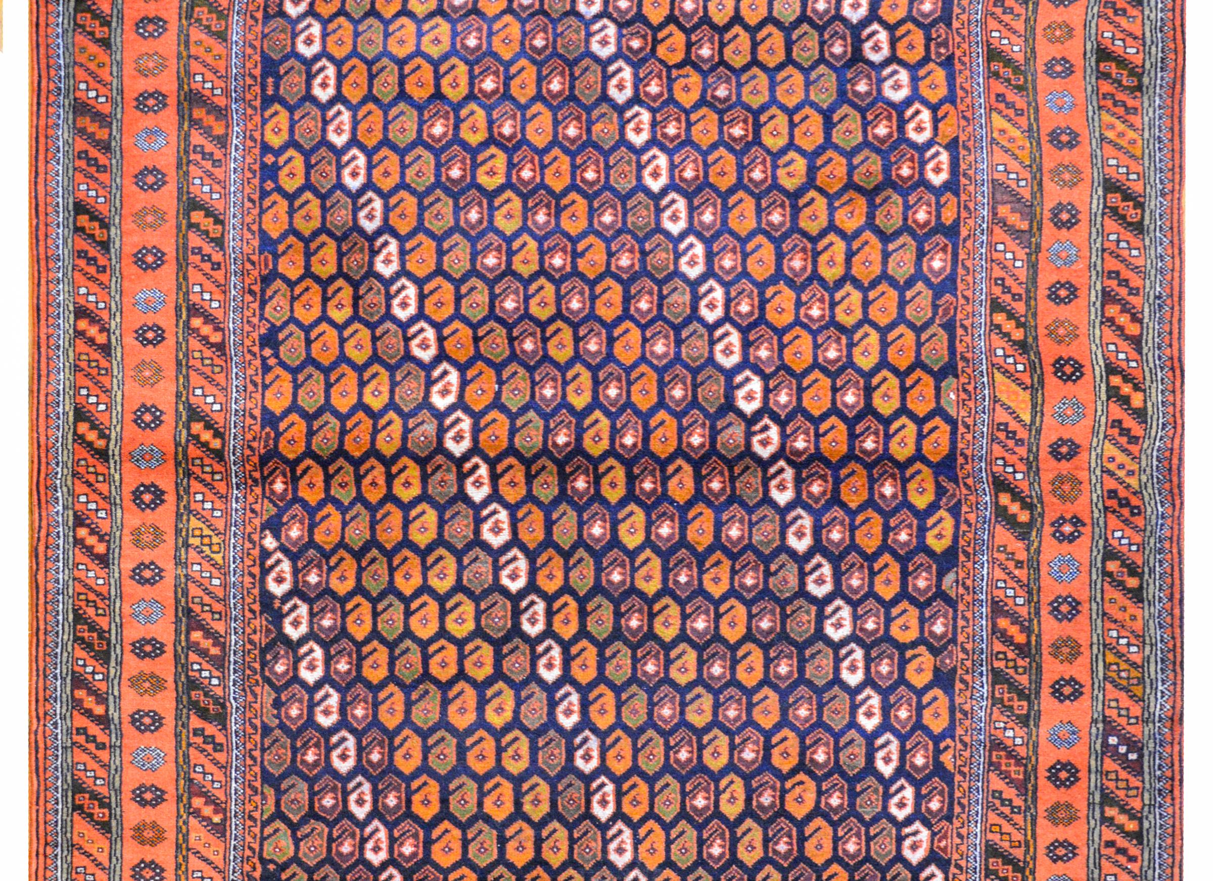 A wonderful early 20th century Persian Shiraz rug with an all-over paisley pattern woven in myriad colors including orange, gold, green, white, and various browns, all on a dark indigo background. The border is composed of a central stylized floral