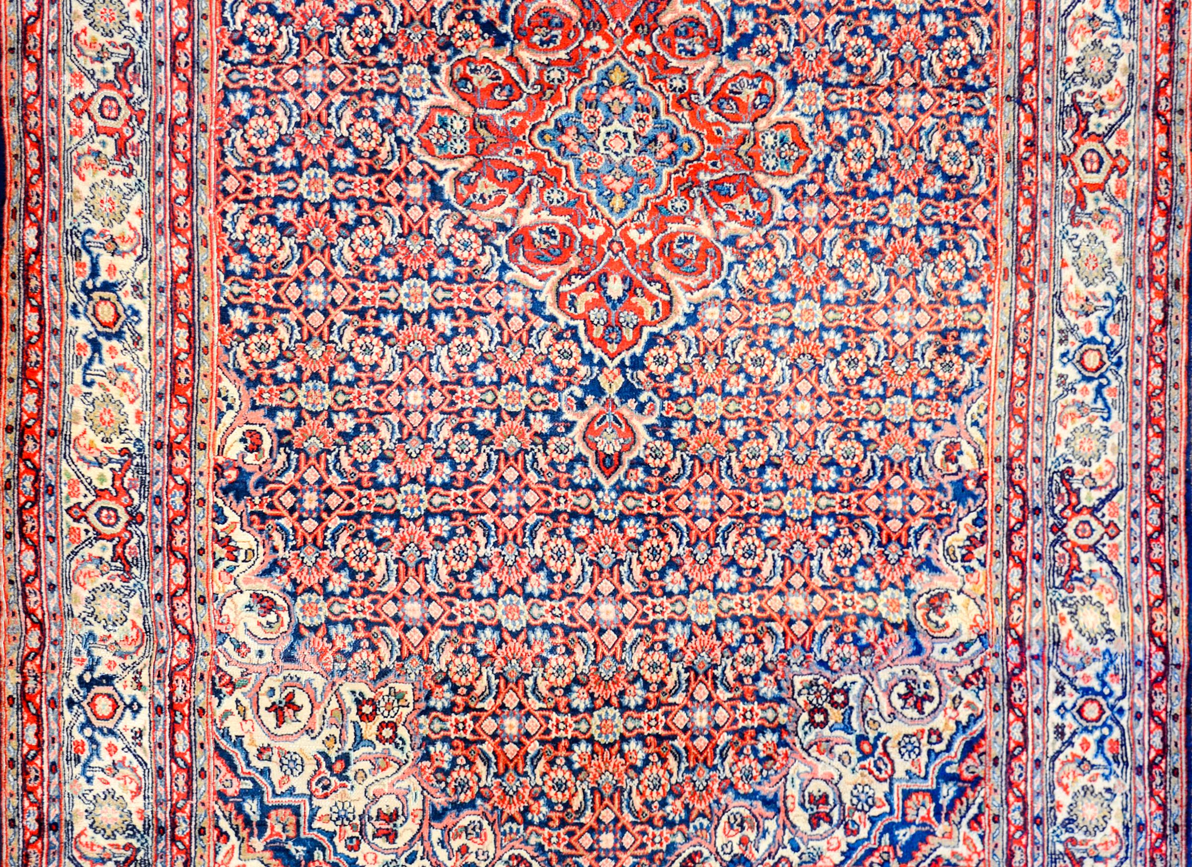 A wonderful early 20th century Persian Tabriz rug with a large red diamond form medallion on a field with an all-over crimson and indigo trellis and floral pattern. The border is wonderful with a wide central floral and vine patterned stripe flanked
