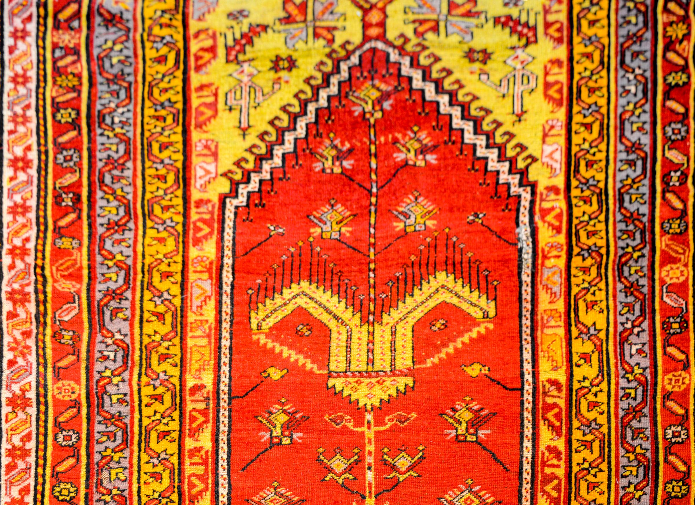 A wonderful early 20th century Turkish prayer rug with a beautiful stylized tree-of-life pattern amidst a field of flowers on a bold crimson background surrounded by multiple thin petite patterned stripes woven in multiple colors.