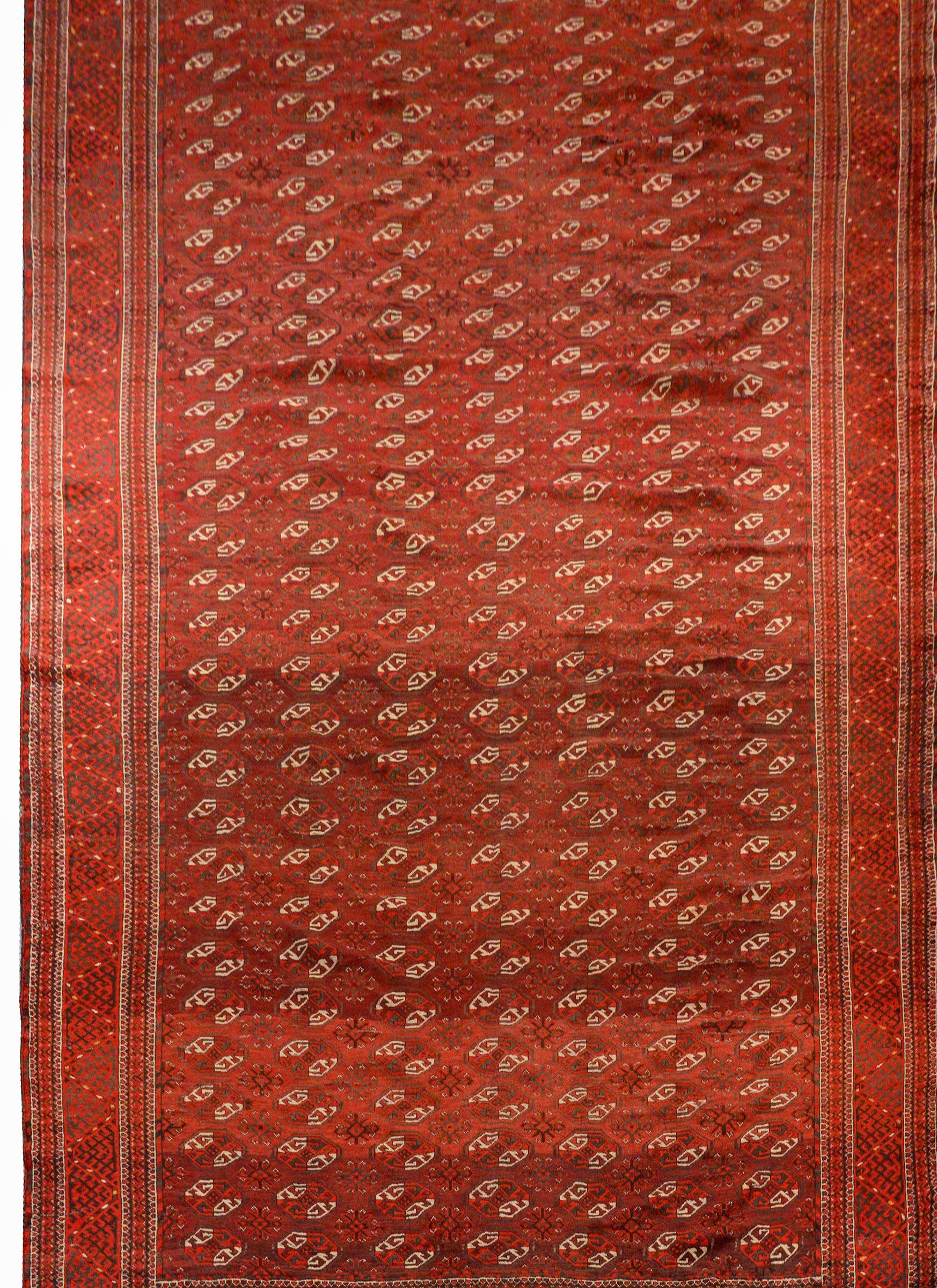 A wonderful early 20th century Persian Turkomen rug with an all-over pattern of crimson and white lozenge-shapes medallions on a crimson background, surrounded by an exceptional geometric stylized meandering motif patterned border.