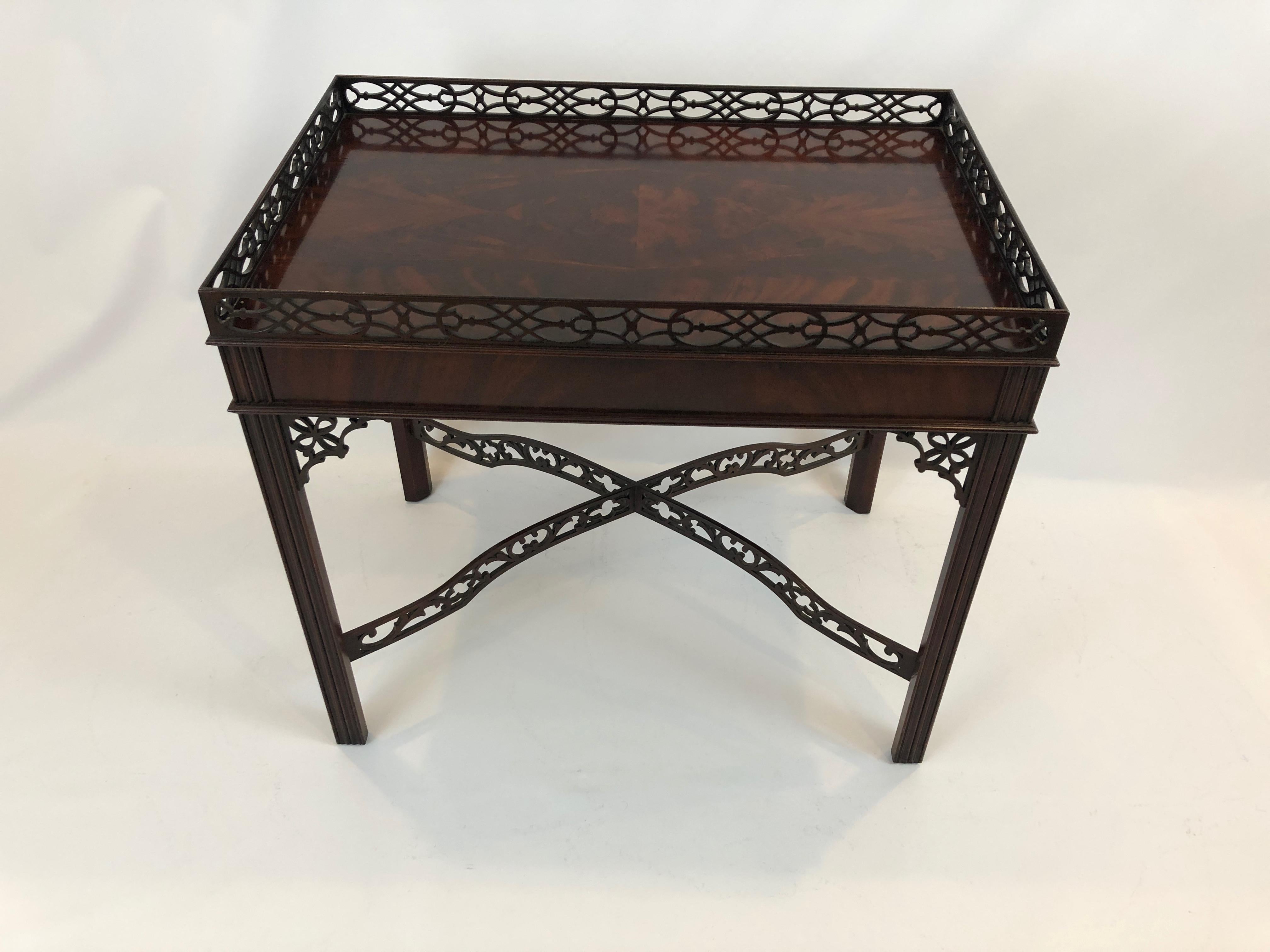 A beautiful Chippendale style rectangular side or tea table having two slides on each end and magnificently crafted wooden fretwork gallery, stretchers and decorative corners under the top. The flame mahogany of the surface is breathtaking. 
Baker