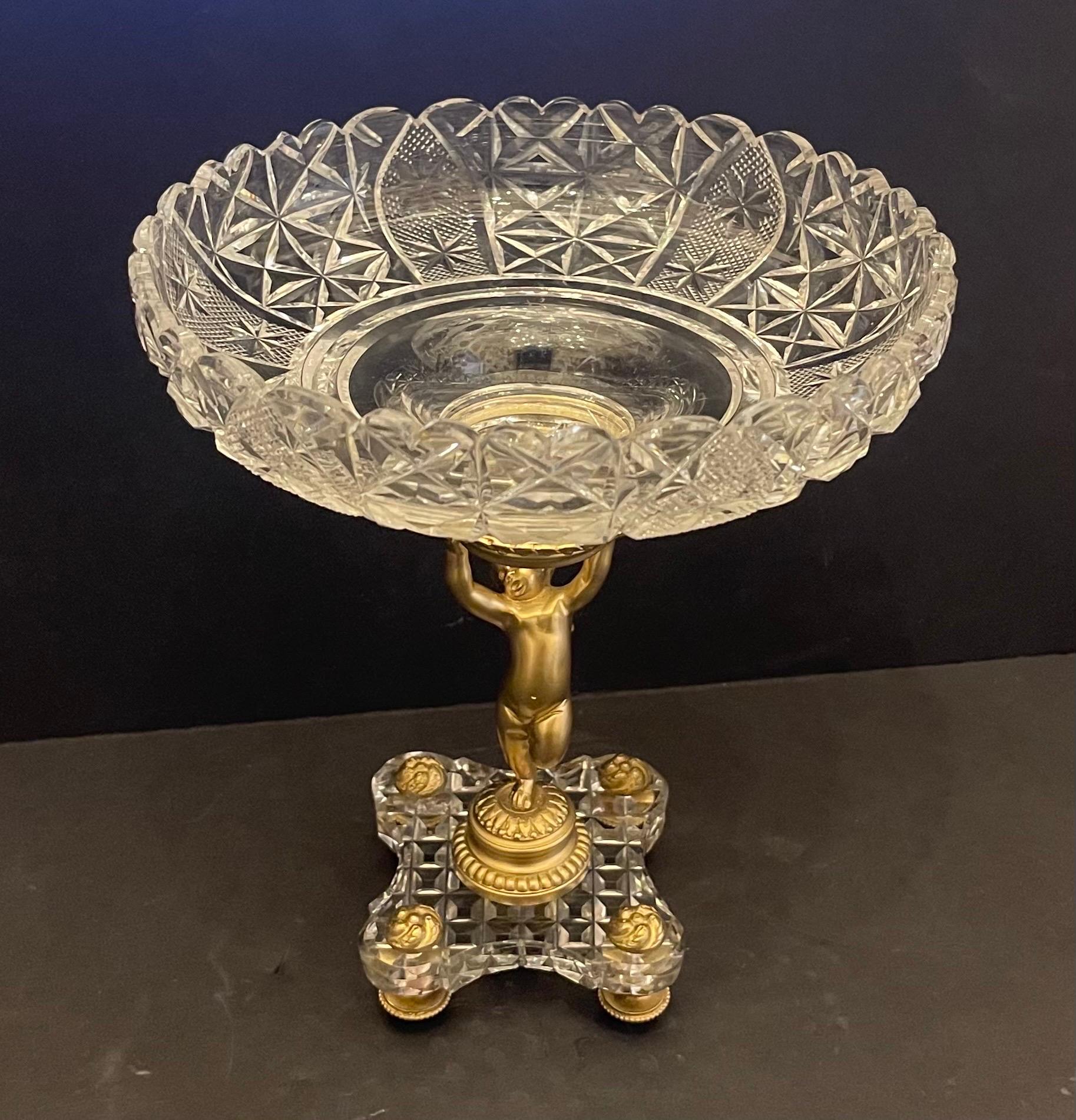 A Wonderful French What We Believe To Be Baccarat Bronze & Crystal Ormolu Cherub / Putti Compote, Centerpiece That Is Depicting A Cherub Holding A Large Cut Crystal Bowl Standing On A Faceted Crystal Base With Four Bronze Feet.