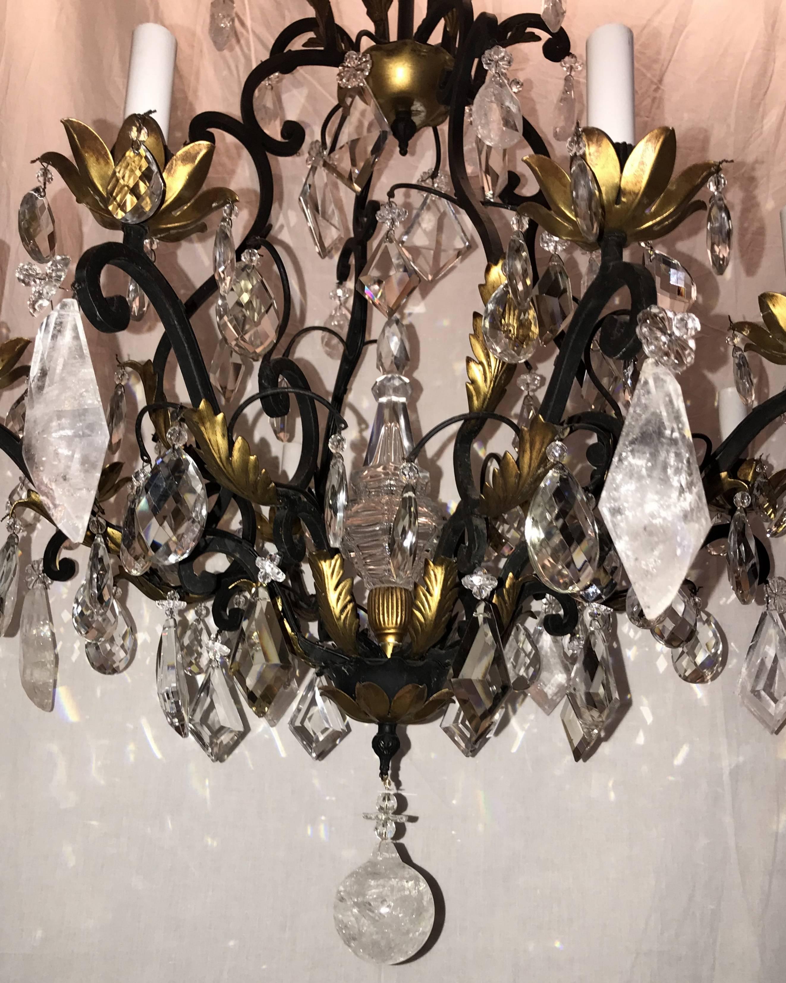 This transitional gilt metal / iron chandelier with eight candelabra lights has wonderful rock crystal prisms, triangular shaped and diamond shaped crystal prisms. There is a large crystal spire that is in the centerpiece of this beautiful