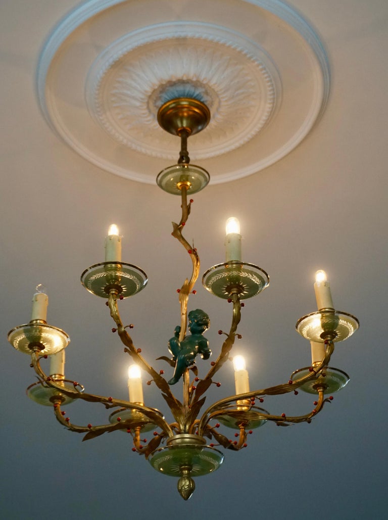 Classical elegant and discrete chandelier counting eight brass gilded arms supporting emerald green Murano glass cups. The arms are decorated with red colored berries surrounding an intense dark green angel figure (putti cherub) creating a subtle