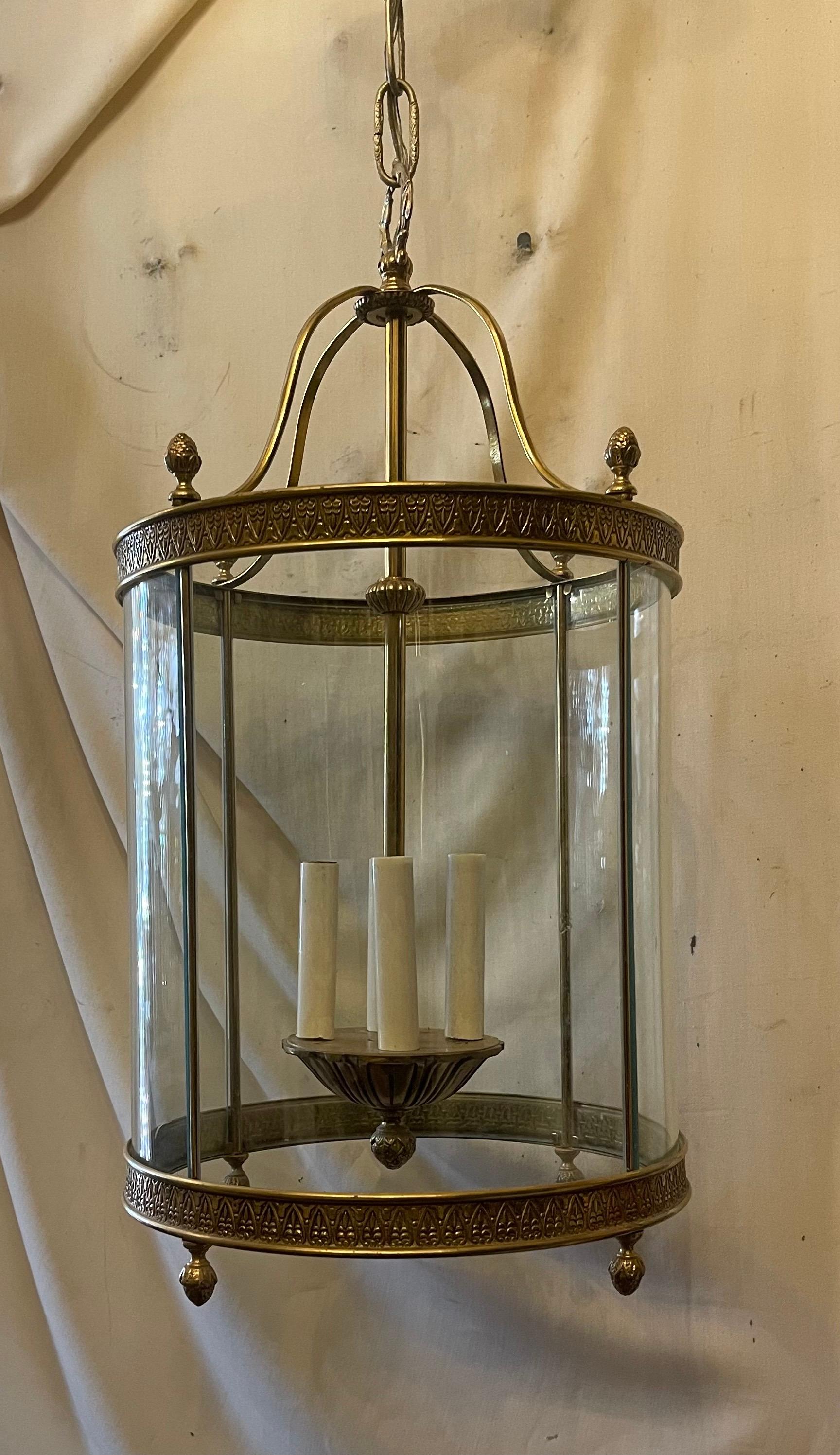 Una elegante linterna de bronce de cuatro luces con adornos de bronce grabado en la parte superior e inferior de la linterna alrededor de unos paneles de cristal curvado. La luminaria tiene 4 brazos de candelabro con un bello racimo de detalles de