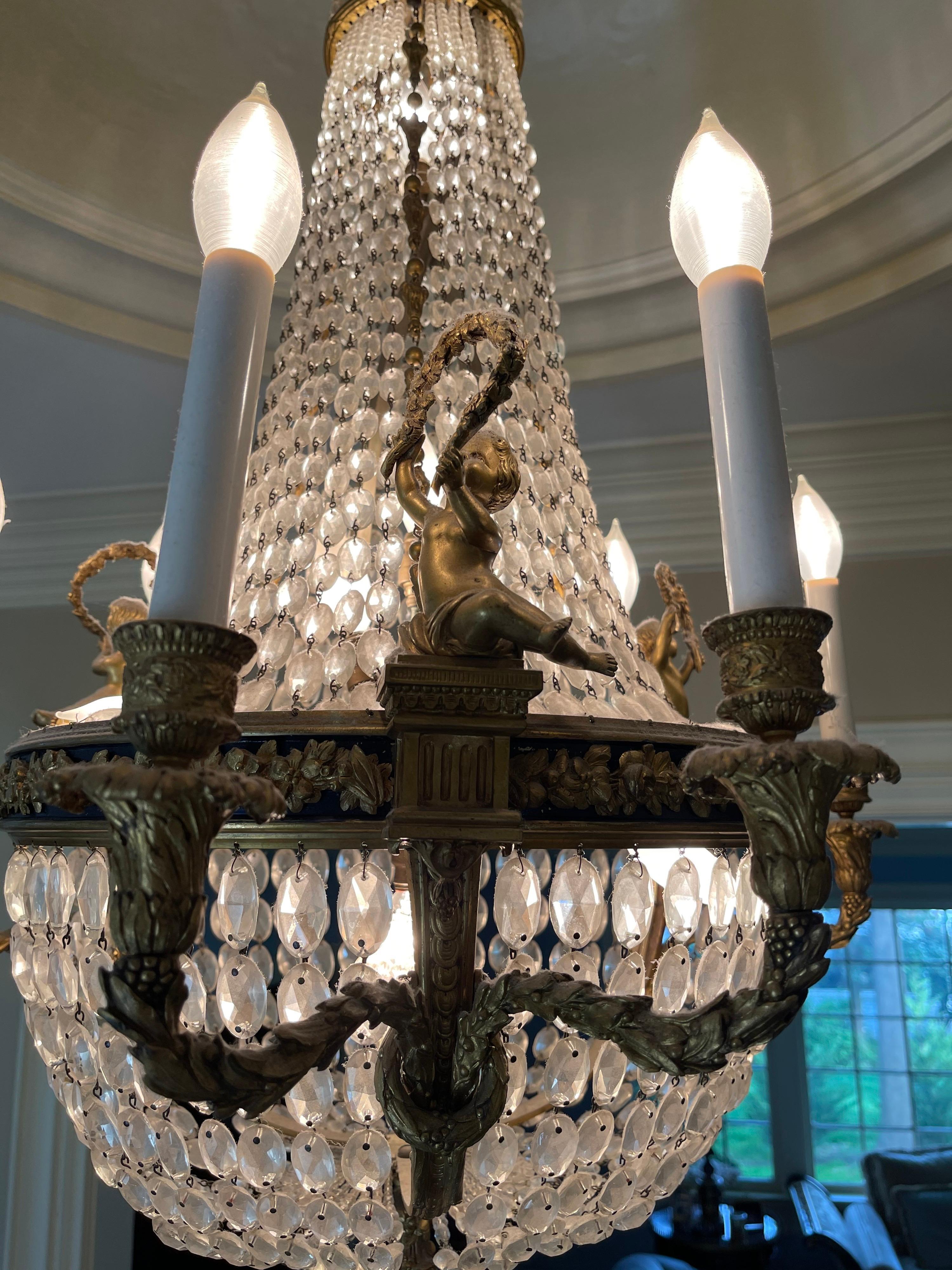 A wonderful French dore bronze & patinated & graduating crystal strand basket chandelier with cherub / putti each holding a garland wreath in the manner of Louis XVI, chandelier has 6 candelabra branch lights on the outside and 7 internal lights.