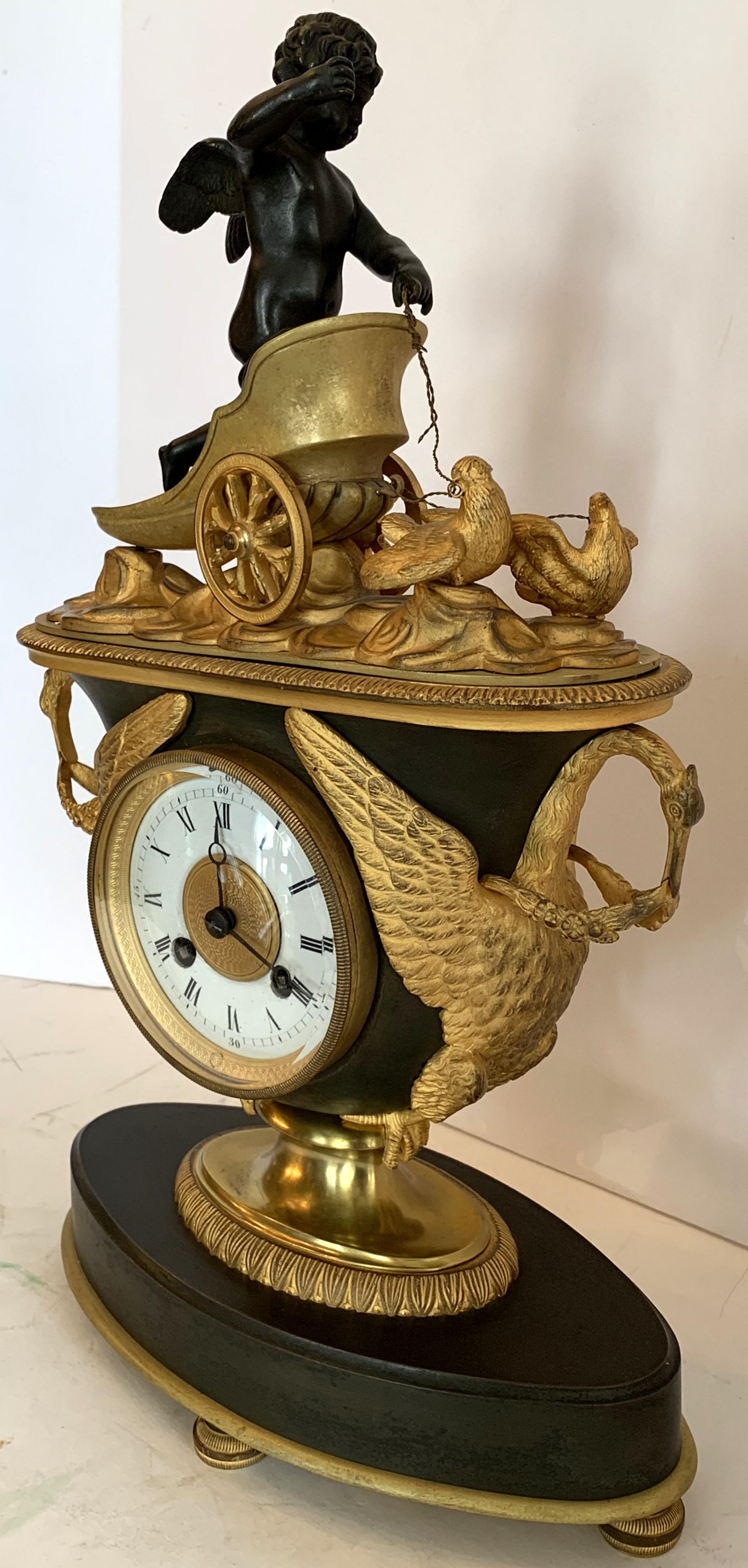 A wonderful French Empire gilt and patinated bronze clock adorned with a cherub riding in a chariot pulled by chickens over a swan handle urn sitting on an oval base, clock is currently working but not guaranteed.