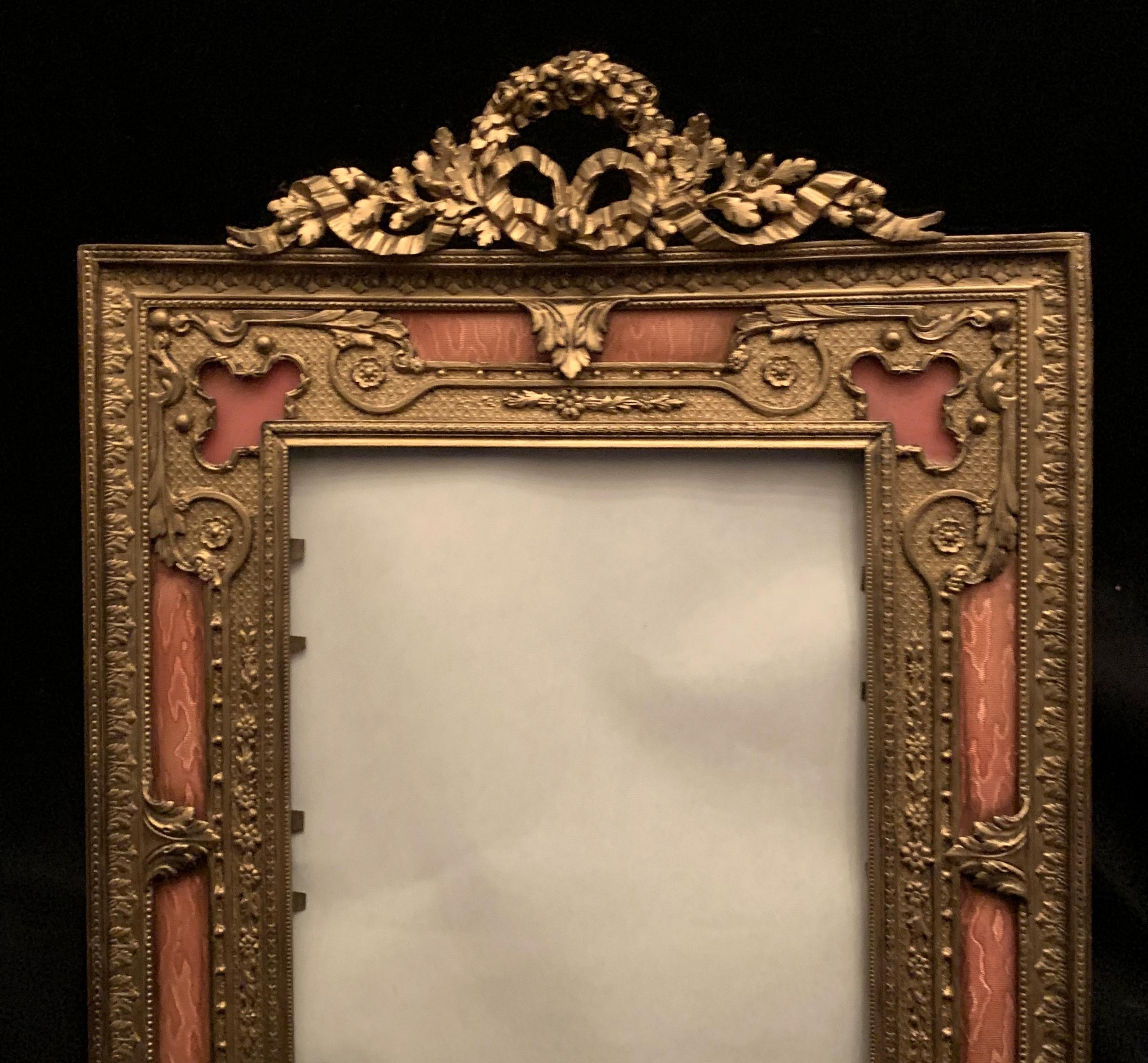 A wonderful French gilt bronze and salmon or pink enamel bow top picture frame with easel back.