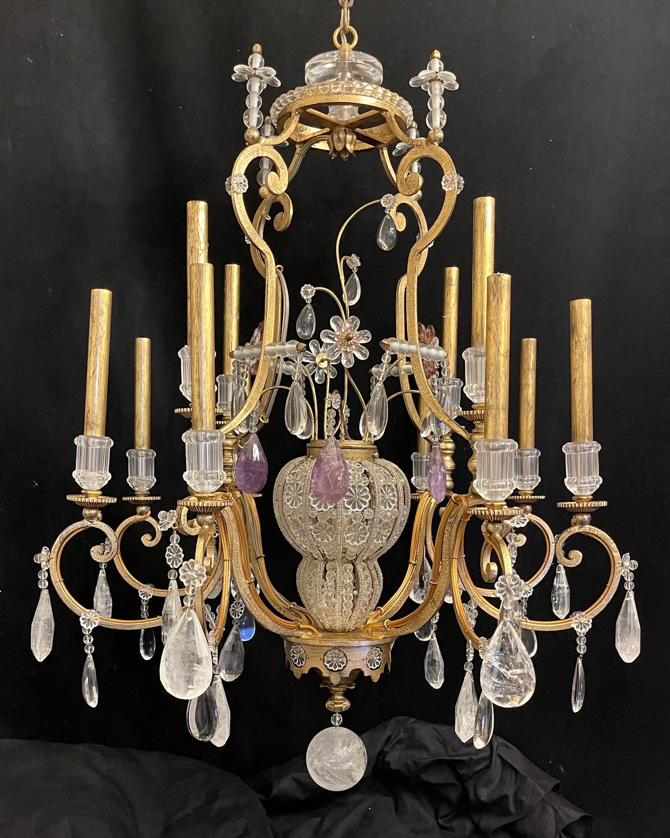 This large scale, stylish and chic rock crystal chandelier was created by the iconic firm of Maison Baguès and is in the Louis XV style with its 12 candle lights and the interior crystal beaded cage has a single bulb. The steel frame is an antique