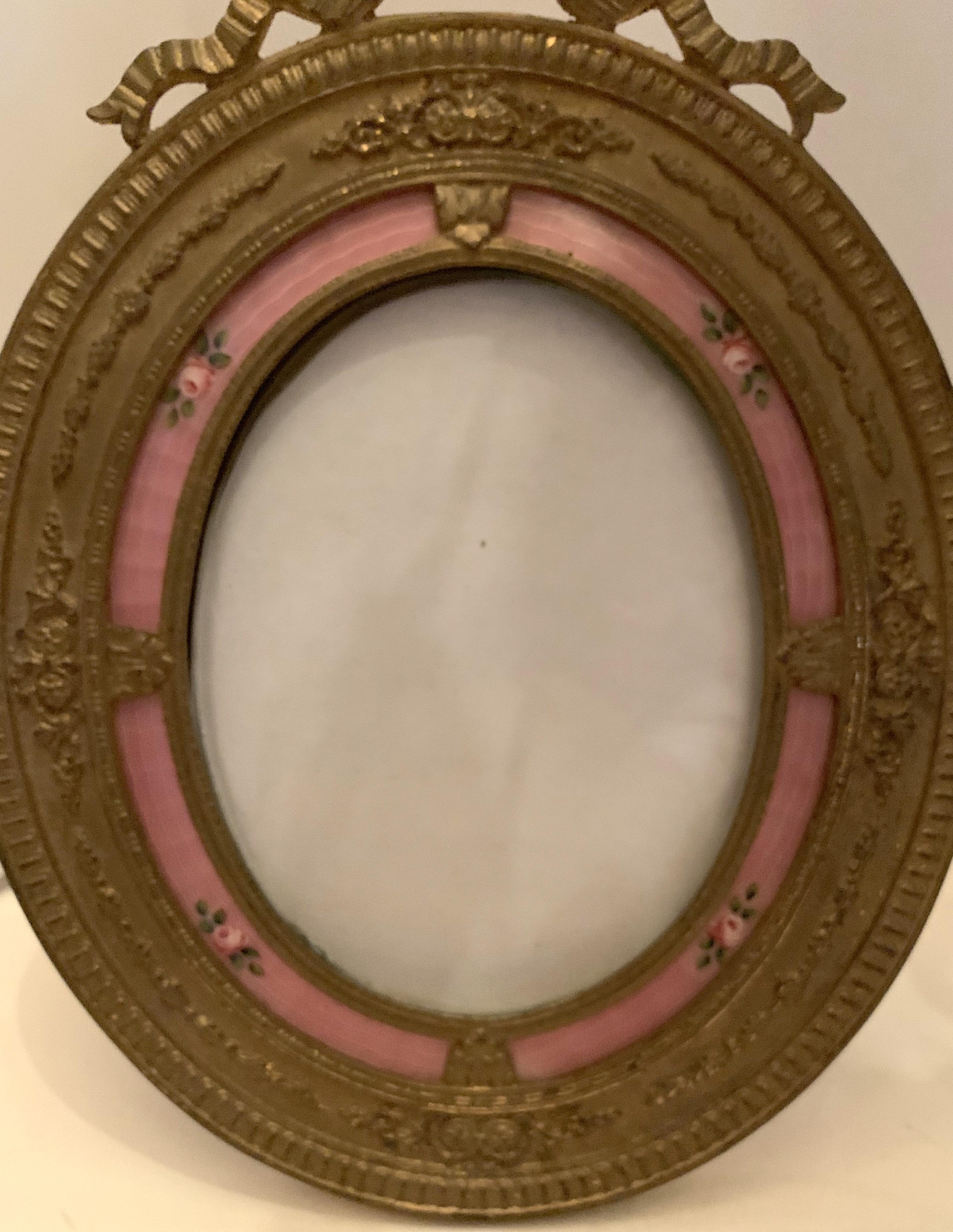 A wonderful French oval bronze and salmon pink enamel and flower decorated bow top picture frame.
