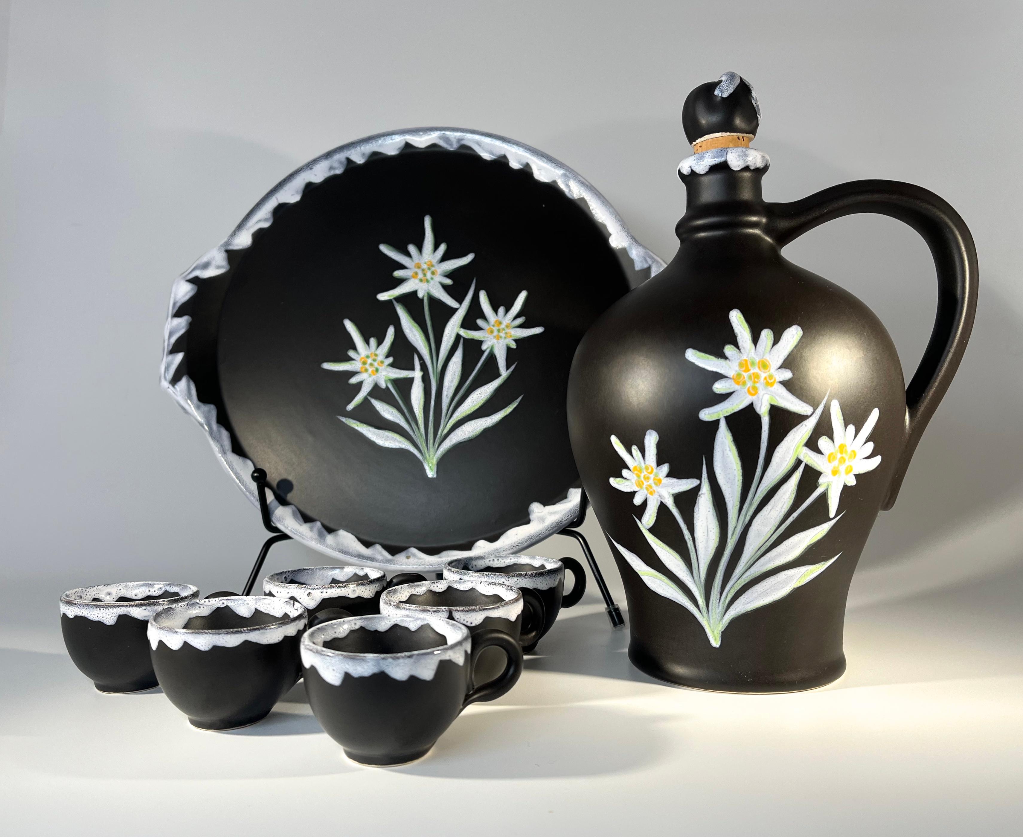 Celebrated ceramicist Gabriel Fourmaintraux  black and white ceramic liqueur decanter, cups and tray set
Elegant hand painted Edelweiss flowers adorn the decanter and tray 
Six petite companion cups, black with white lava rims
Circa 1950's  
Signed
