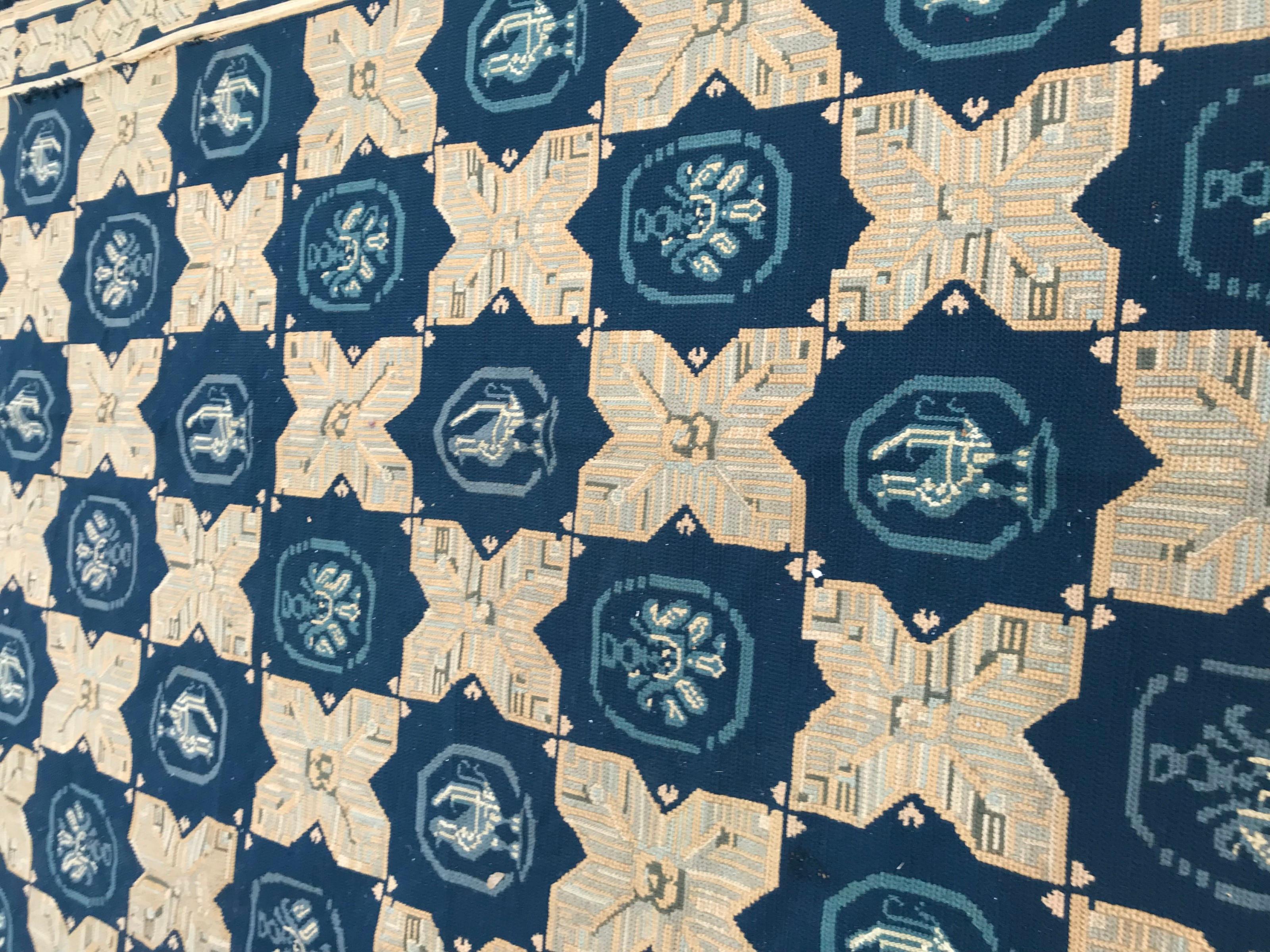 Découvrez l'élégance de notre tapis portugais à l'aiguille Arraiolas du début du XXe siècle. Ornée d'un captivant design géométrique victorien dans des tons apaisants de bleu et de beige, cette pièce exquise est méticuleusement brodée à la main avec