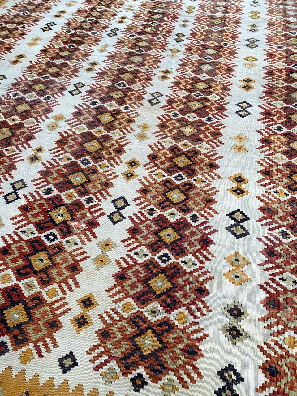 Exquisite large Kilim featuring a captivating geometrical design in vibrant colors such as yellow, orange, green, and dark purple. Meticulously handwoven with wool on a cotton foundation. The white background showcases stylized and repetitive