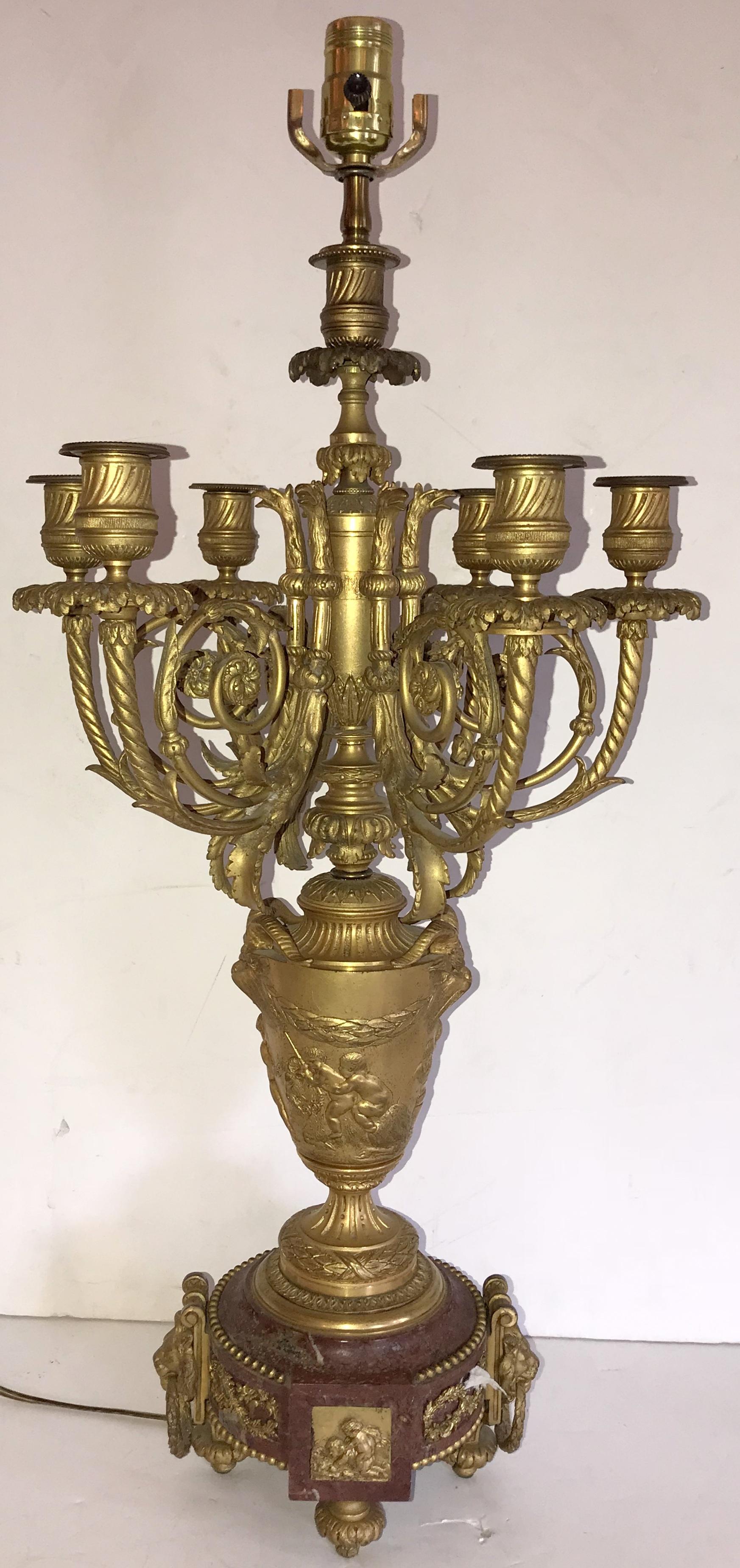 An exquisite large pair of 19th century Louis XVI ormolu and Rouge marble candelabra lamps. Each candelabra is raised on a round Rouge Griotte marble base on ormolu feet with lion ormolu mounts. Above, each superbly chased ormolu urn portrays a