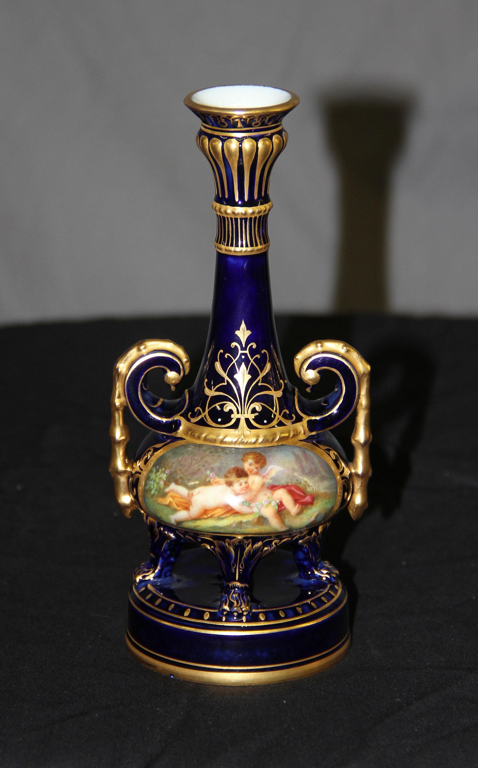A wonderful little Vienna style porcelain vase.

With an oval picture depicting two cherubs at play with raised gold designs, fluted neck and lion paw feet standing on a round base.
