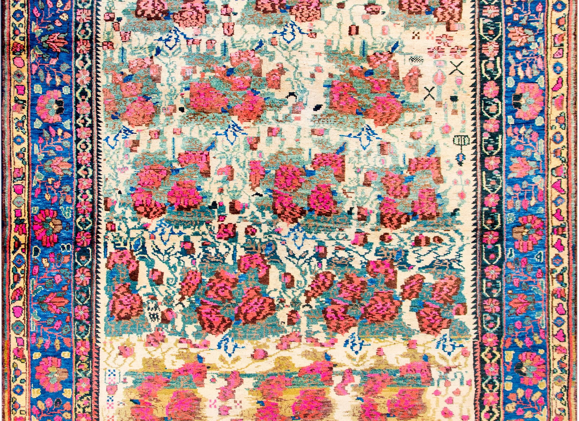 A wonderful mid-20th century Persian Afshar rug with a beautifully woven pattern of bright pink flower clusters, amidst a field of vines and myriad flowers on a cream colored background. The border is complex with multiple floral and vine patterned
