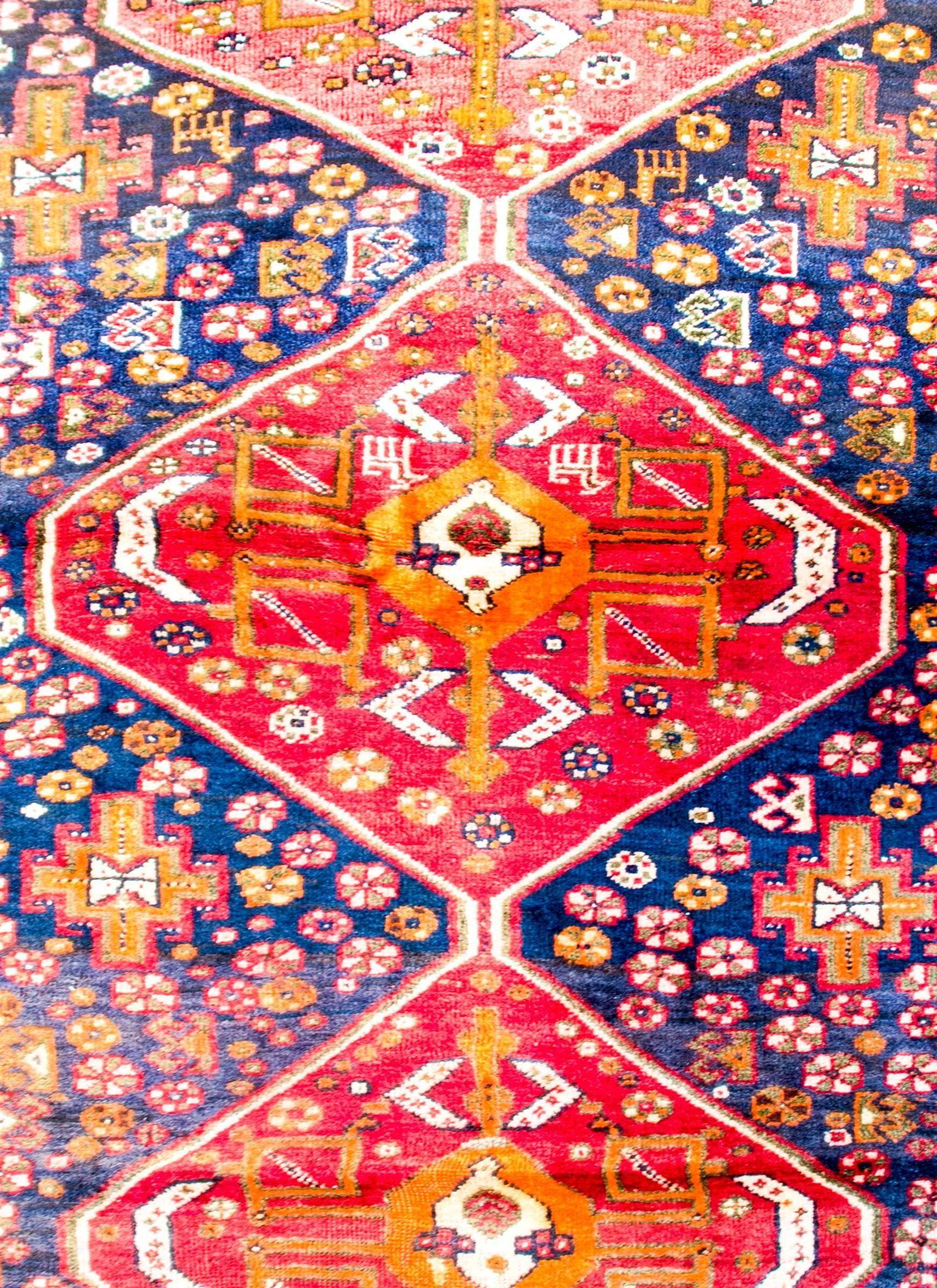A brilliant mid-20th century Shiraz rug with an incredibly woven pattern containing three large central diamond medallions, each with multiple stylized flowers, all woven in crimson, white, and gold, on bright crimson backgrounds. The medallions