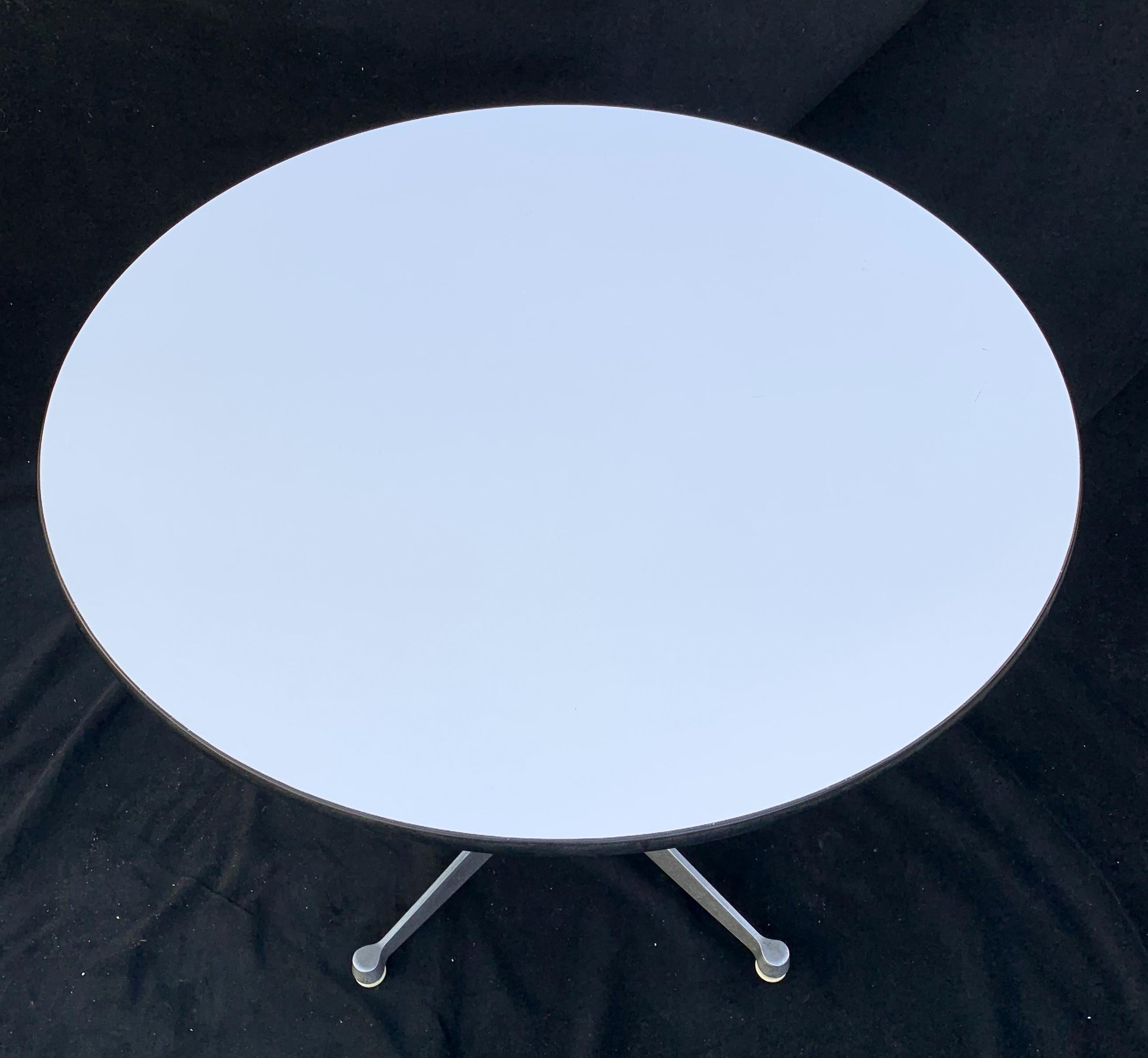 A wonderful Mid-Century Modern Herman Miller round pedestal table having a white laminate top and trim around the outer edge and supported by a black center pole with an aluminum four leg Stand
Herman Miller decal and 