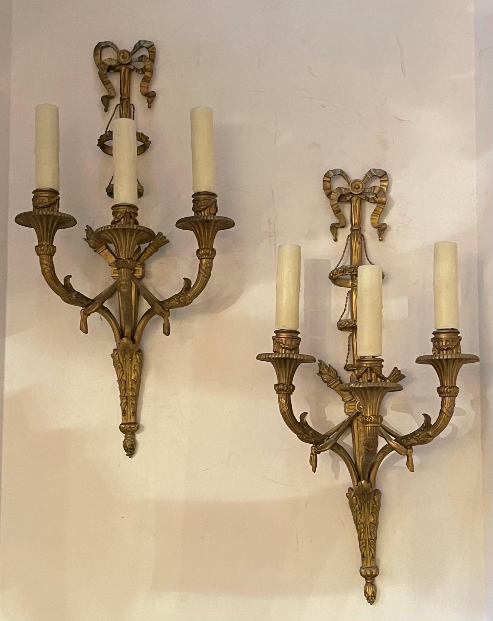 A wonderful pair of French gilt Doré bronze bow top cross Torchiere three candelabra light wall sconces with swag and baskets on the center stem in the manner of E. F. Caldwell.