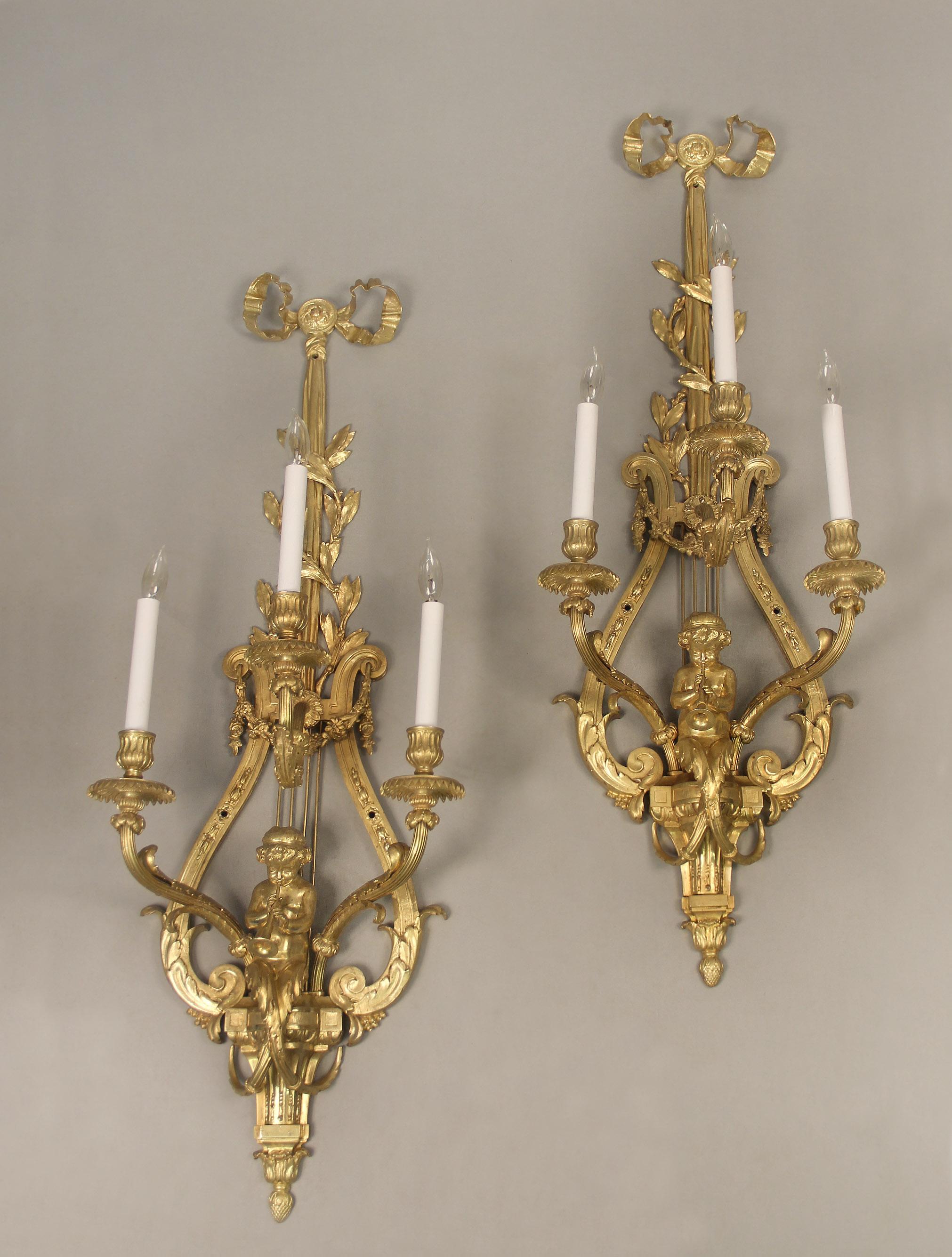 A wonderful pair of late 19th century gilt bronze three light cherub sconces

Each with ribbon-tied top above a lyre form backplate with swags of flowers, three foliate scrolling candelabra arms, centered by a large trumpet playing putti, leading