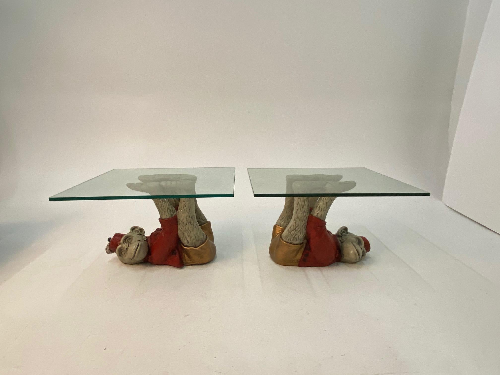 Show stoppingly fun whimsical pair of vintage monkey motife end tables having cast plaster painted apes dressed in red bellhop outfits lying in fantastic acrobatic positions on their backs, with extended arms and legs that support glass table tops.
