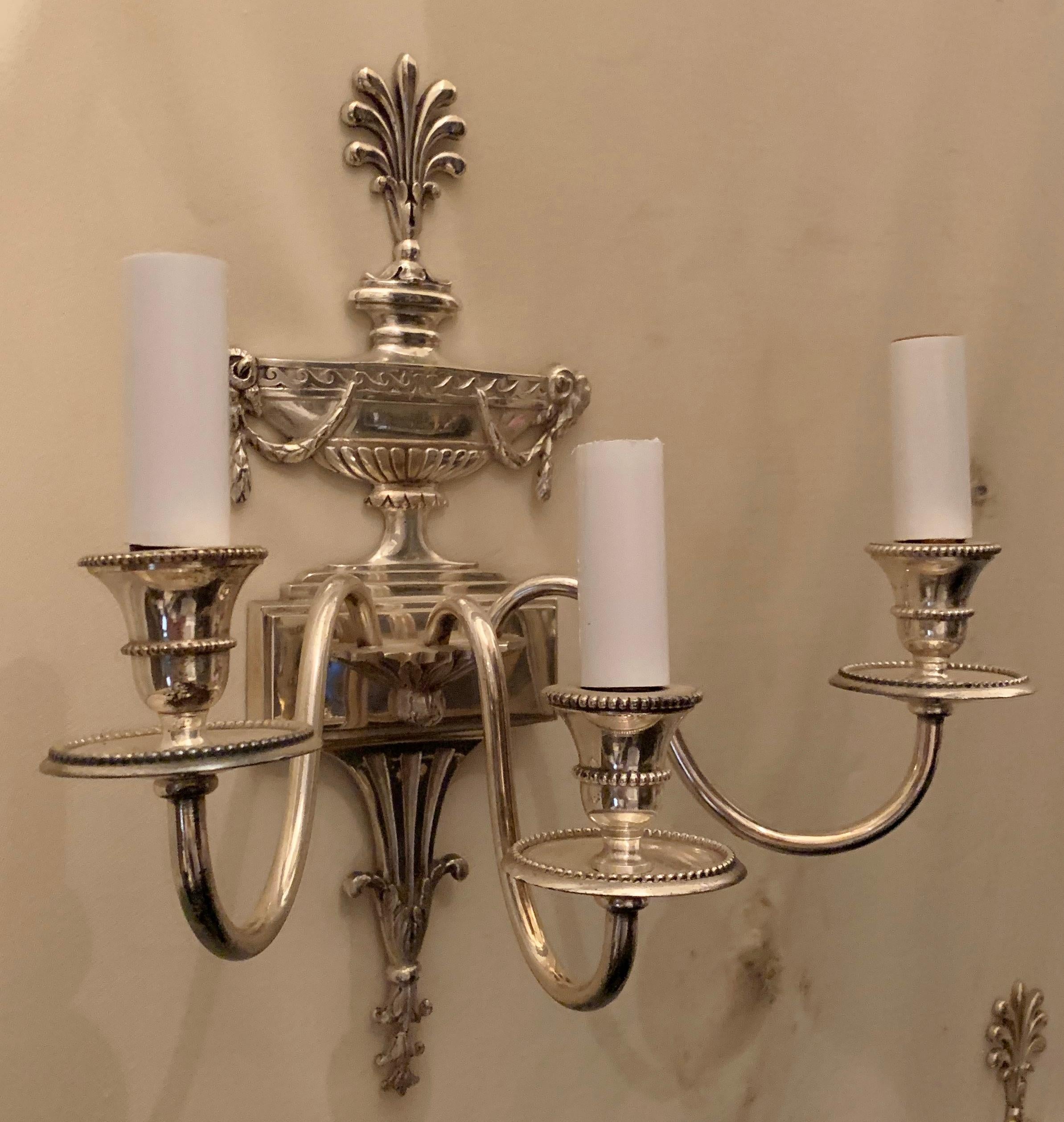 A wonderful pair of silvered / polished nickel bronze sconces with a Baguès Paris label in the back in the neoclassical design with urns and ram's head back plate and three candelabra sockets each, in the manner of E.F. Caldwell.