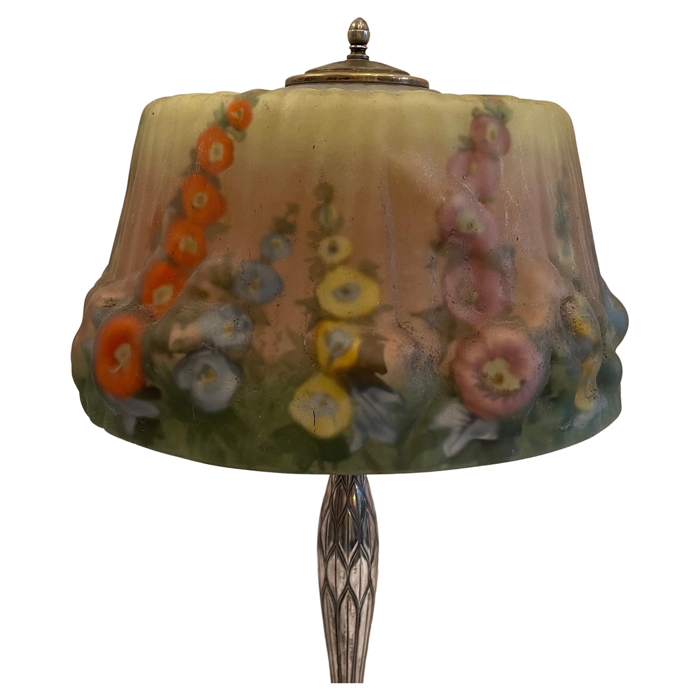 A wonderful Pairpoint Puffy Hollyhock table lamp, c. 1920's. This beautiful Pairpoint puffy shade depicts hollyhocks in full bloom against a cheerful background. Hollyhocks are painted in blues, yellows, oranges and purples with a mixture of green