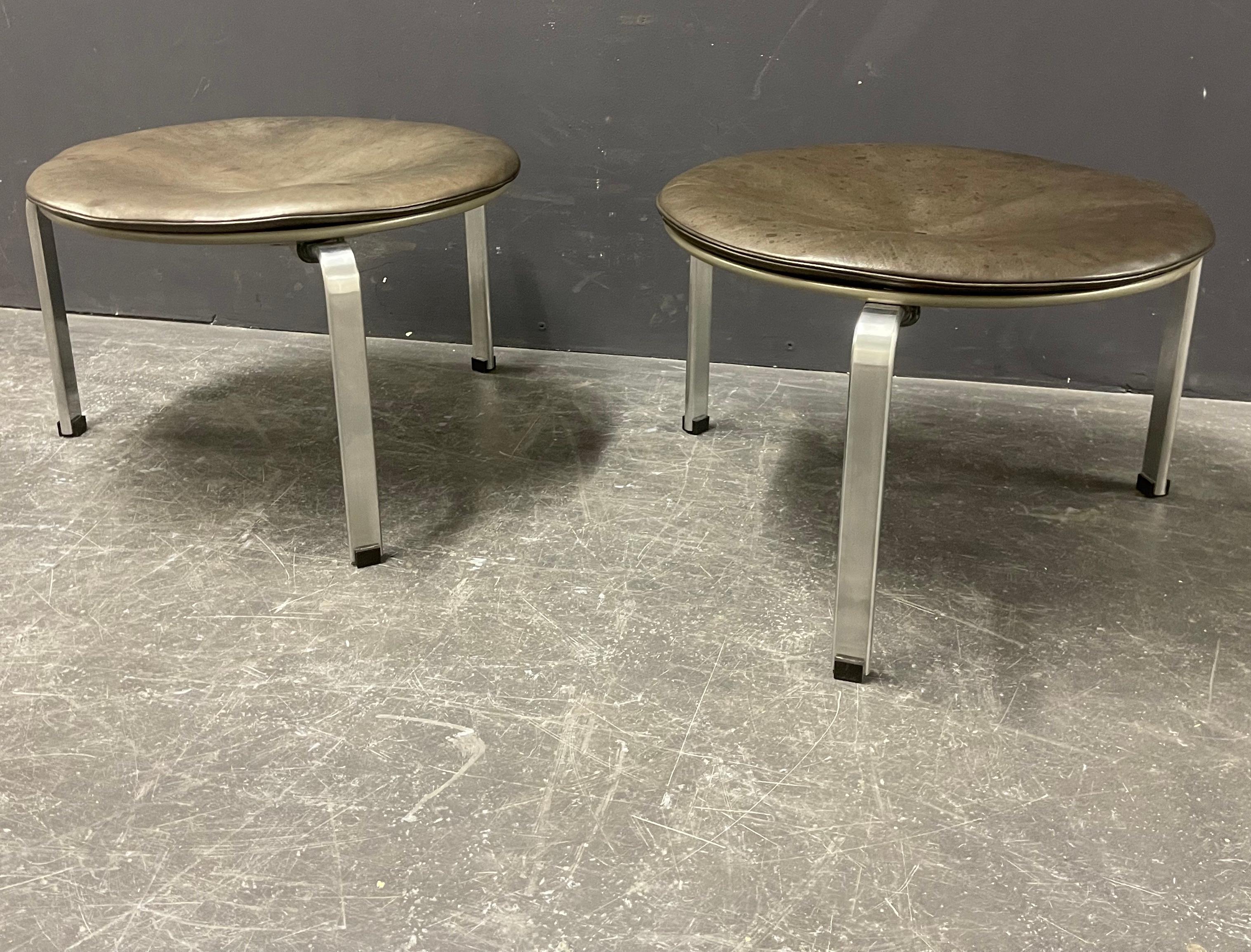 we are very happy to offer these two iconic and wonderful aged pk33 stools by poul kjaerholm. born in black leather these two have turned to a warm brown/grey. steel, plywood, paint and steel is like new. price is for one.