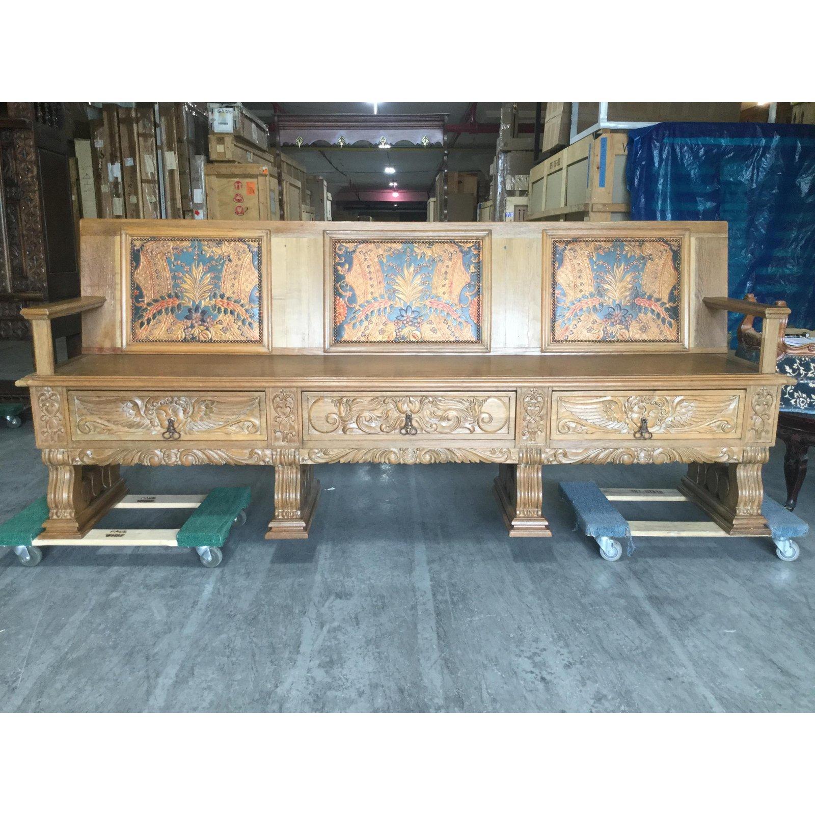 This large oak bench features three Spanish embossed leather panels in gorgeous shades of blue, gold, and green depicting natural flora and fauna. It has three drawers at the base of the seat that are carved with a cherub on the center drawer and