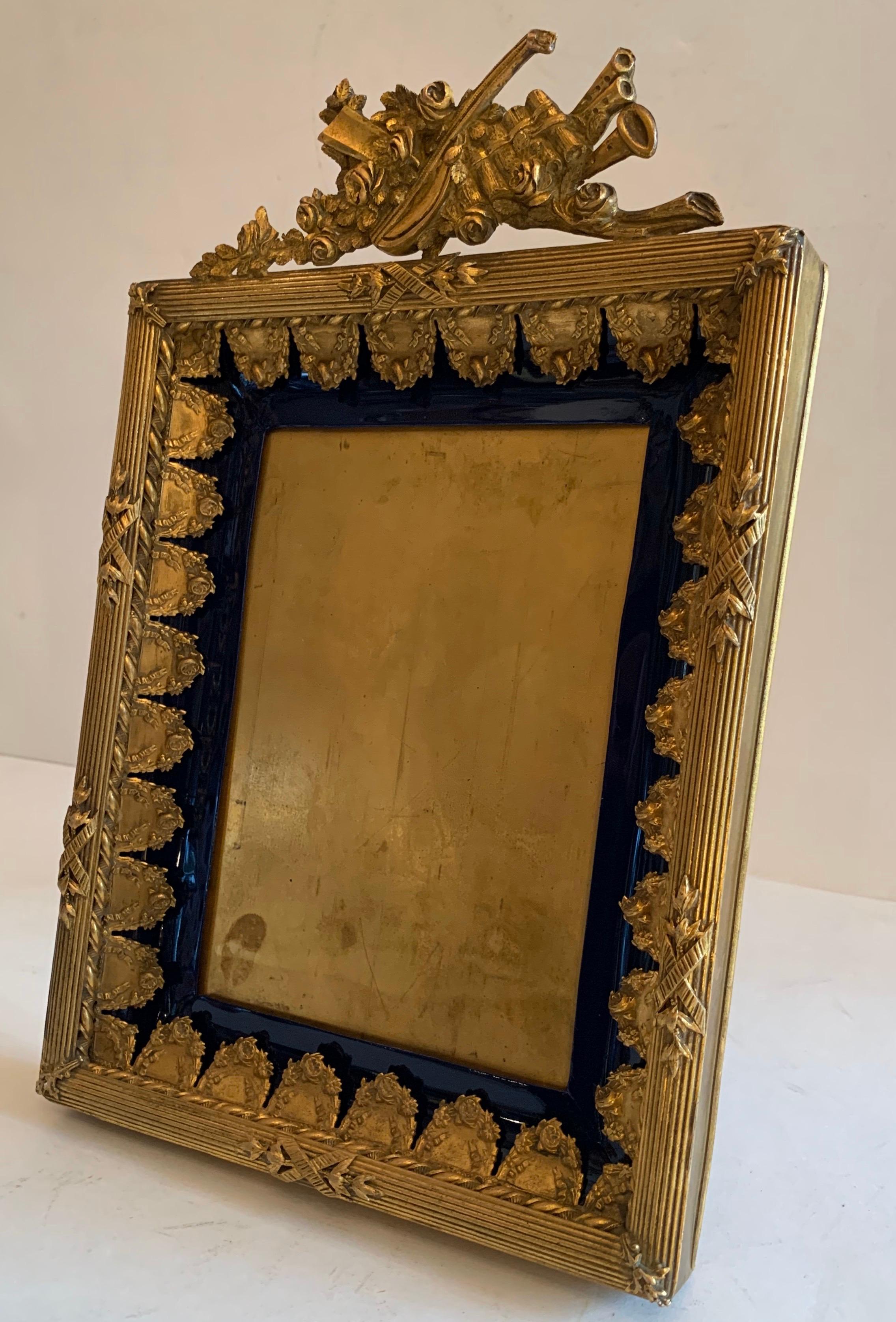 Wonderful rich Royal blue faux enamel and doré bronze French picture frame with beautifully detailed ormolu mounts on musical instruments and floral elements.

Measures: 9.5