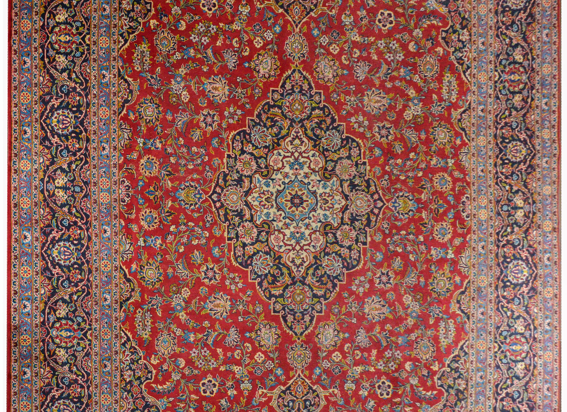 A wonderful early 20th century traditional Persian Kashan rug with a large diamond medallion amidst a field of large-scale flowers on a brilliant crimson background. The border is exceptional with multiple floral and scrolling vine patterns woven in