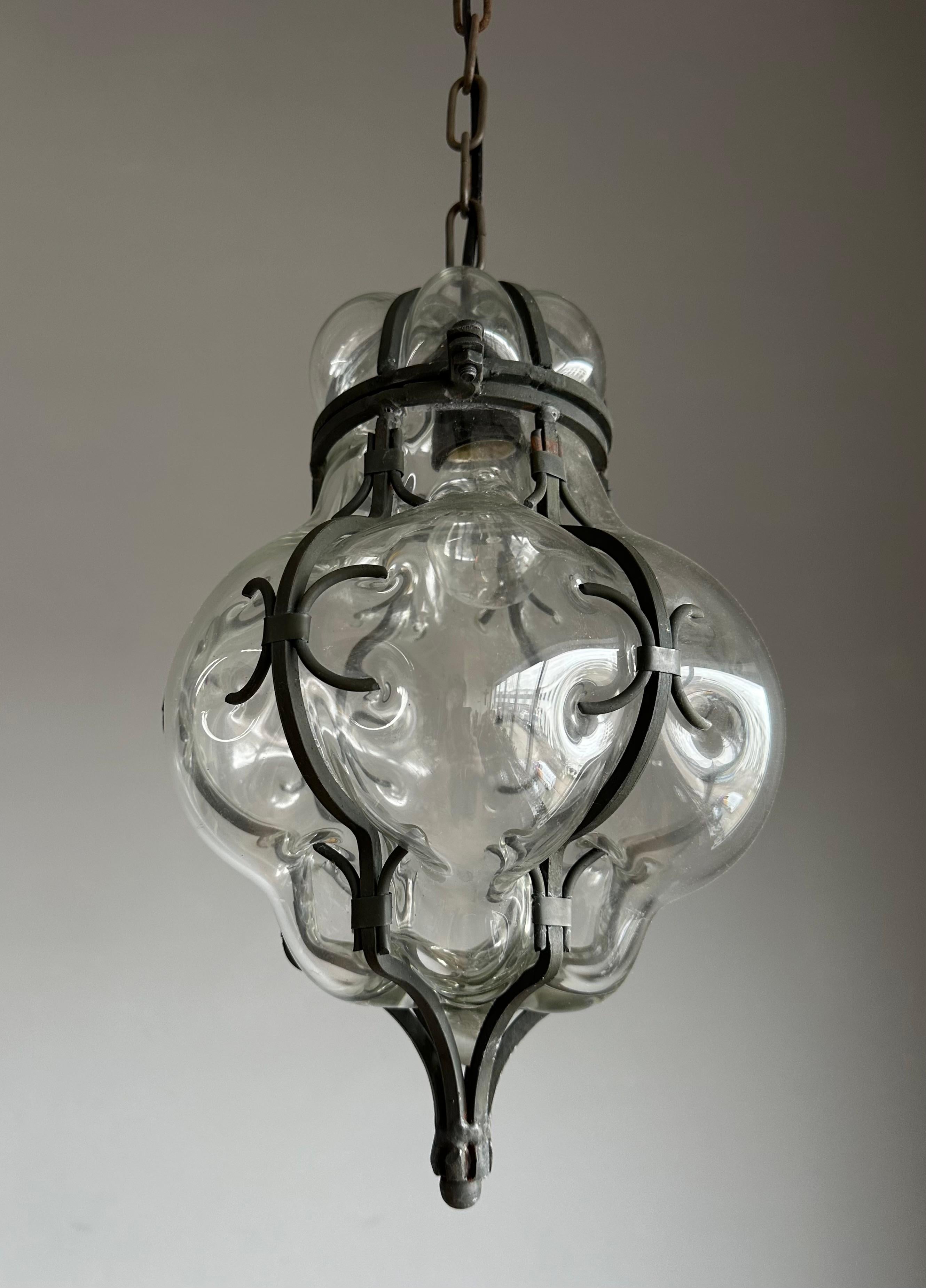 This handcrafted and stylish pendant is in near-mint condition.

This single light, Italian pendant  is very beautiful, both in shape and in color. The stunning clear glass is mouth-blown into a hand forged, wrought iron frame and the result truly