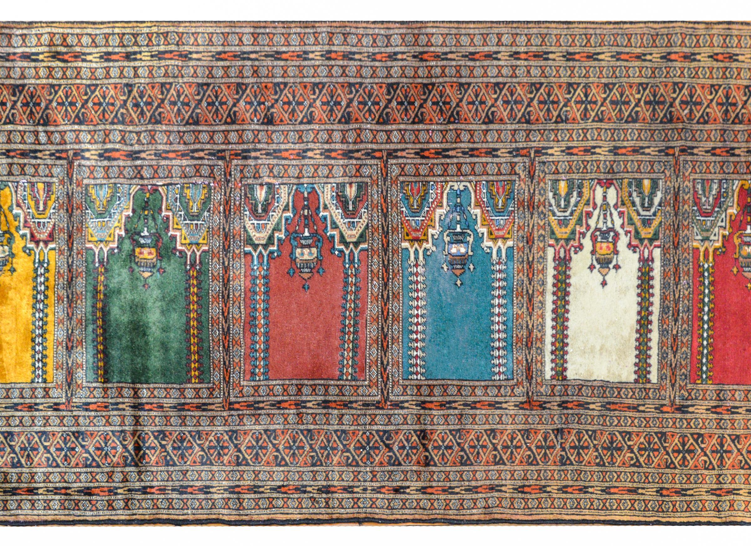 A wonderful vintage Pakistani Bokhara Prayer rug with a brightly colored pattern containing six niches, representing the mihrab of a mosque, and each niche with a pair of matching columns and a hanging mosque lamp. Surrounding each niche is an