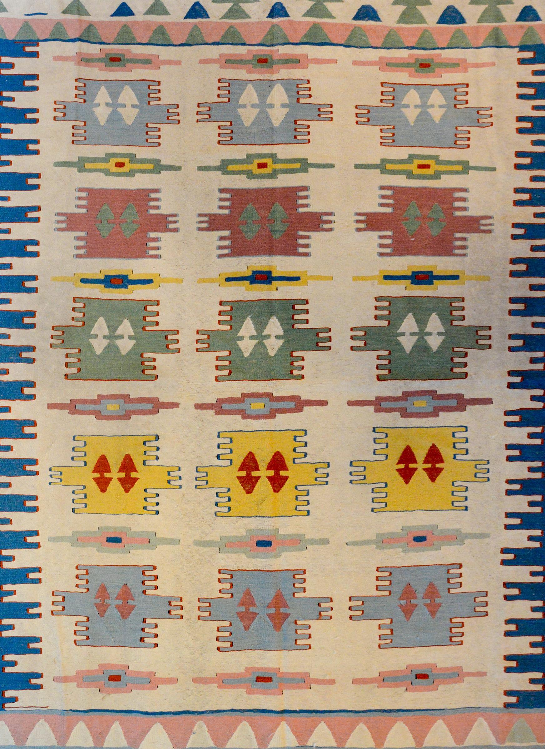 A wonderful vintage Indian Dhurrie Kilim rug with a bold geometric pattern woven in indigo, crimson, green and gold on a natural undyed background surrounded by a fantastic geometric indigo and faded crimson border.