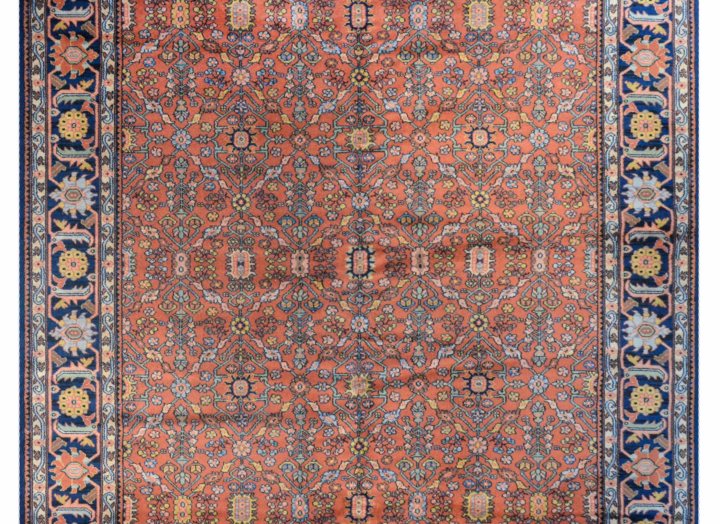 A wonderful vintage American handwoven Karastan Heriz style rug with an all-over trellis pattern woven in coral, gold, light and dark indigo, and pink vegetable dyed wool. The border is wide with a large-scale floral and scrolling vine patterned