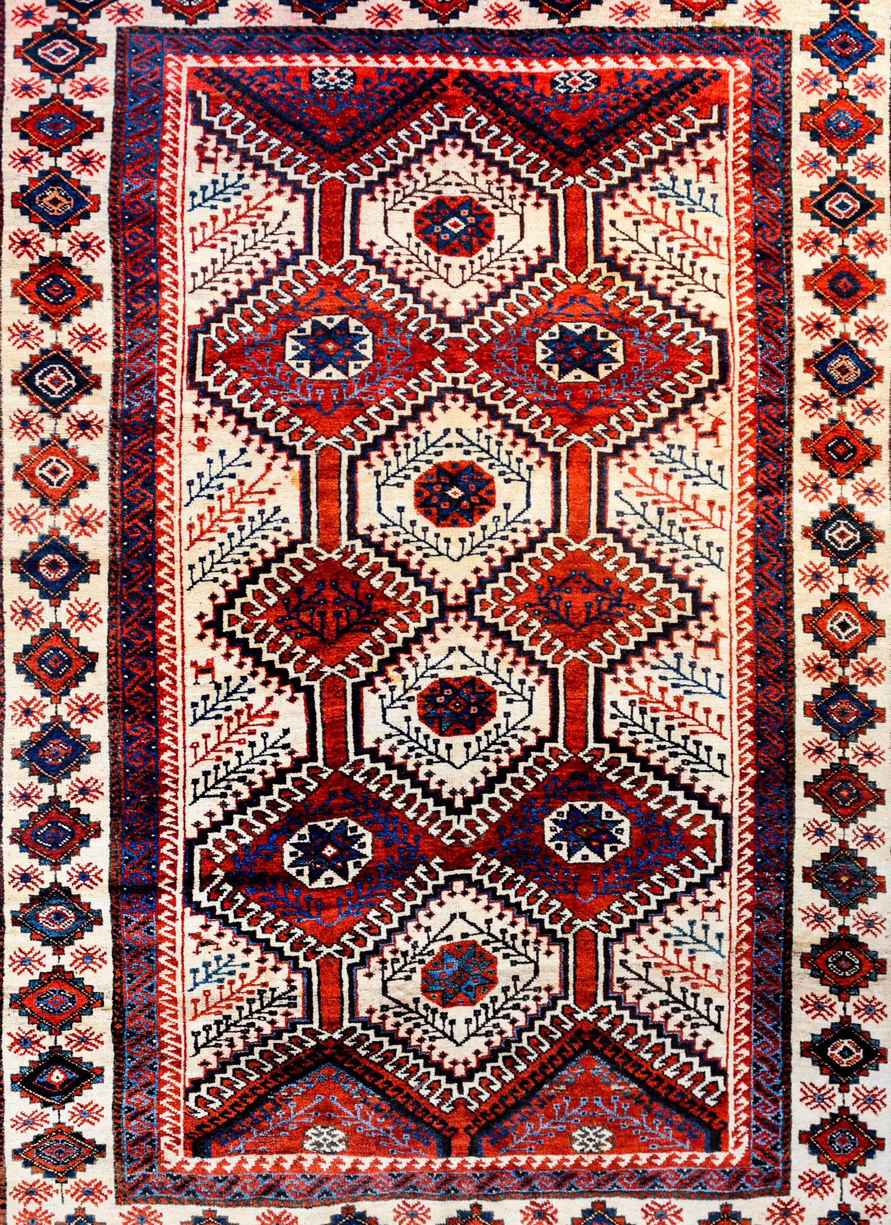 A wonderful vintage Persian Lori rug with a bold tribal pattern containing multiple diamond patterned medallions amidst a crimson and indigo field, all with a stylized petite patterned vine and leaf pattern. The border is exceptional with a wide