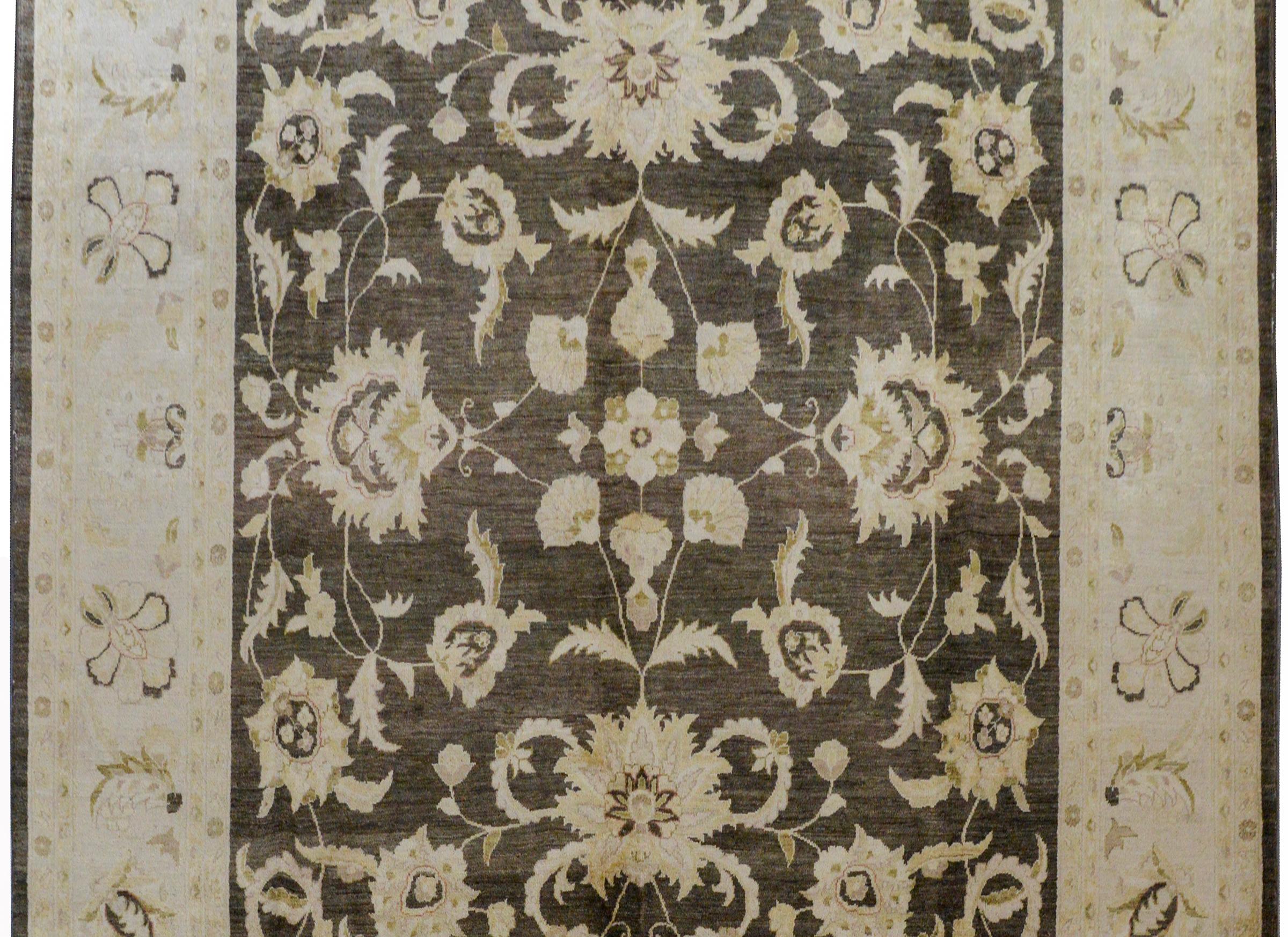 A wonderful vintage Pakistani rug with an all-over field of large flowers and scrolling vines woven in muted greens and golds, on a dark brown background. The border is exceptional with a similarly patterned and colored border but with a cream