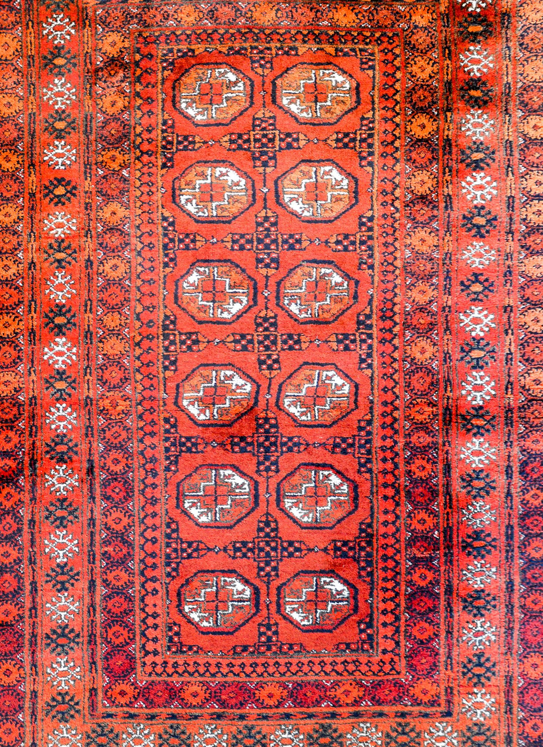 A wonderful vintage Persian Turkoman rug with several medallions in the center woven in orange, white, and indigo dyed wool, surrounded by a rather wide complex border containing several floral and geometric patterned stripes.